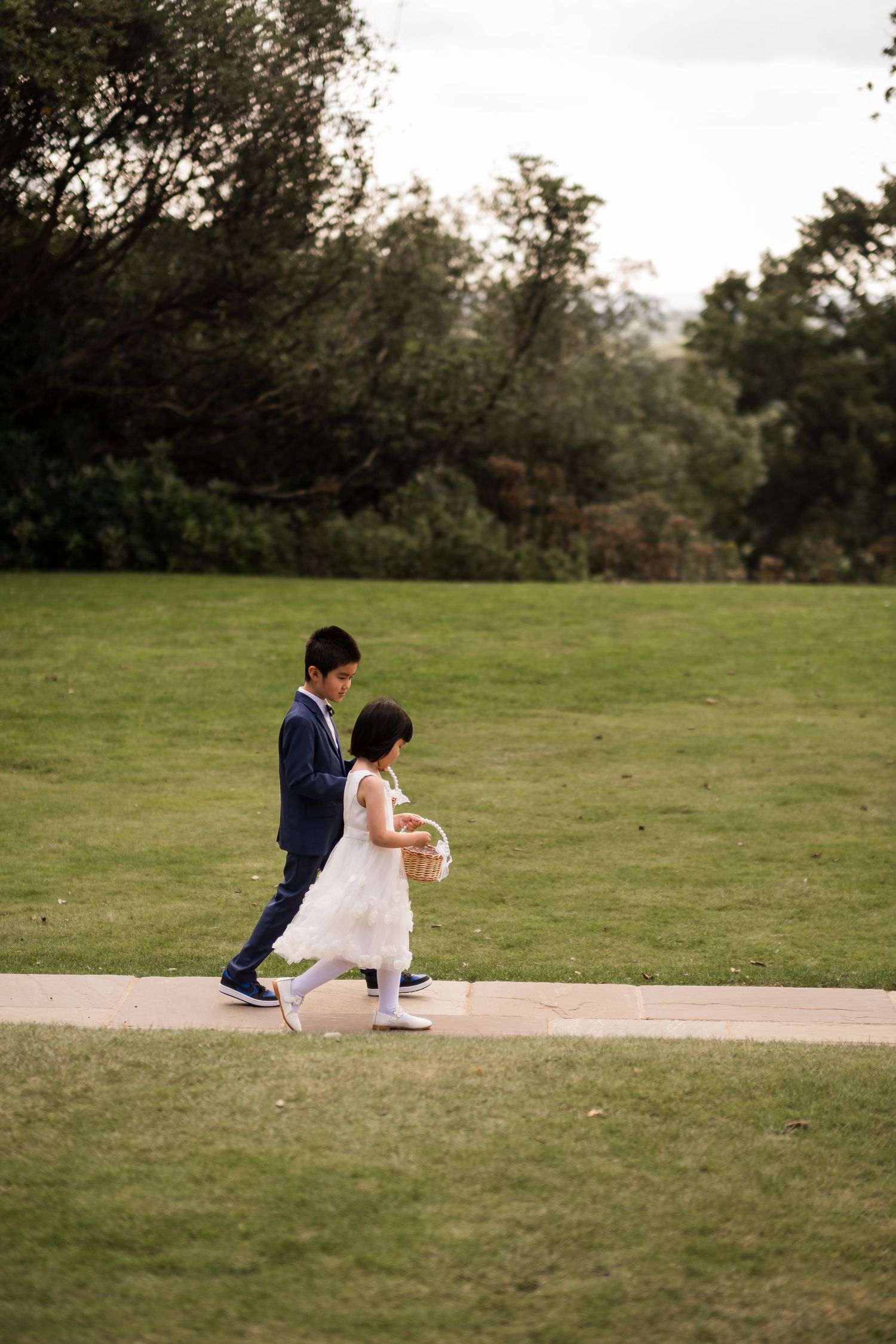 A couple in wedding attire sits together on a concrete ledge overlooking a grassy hillside.