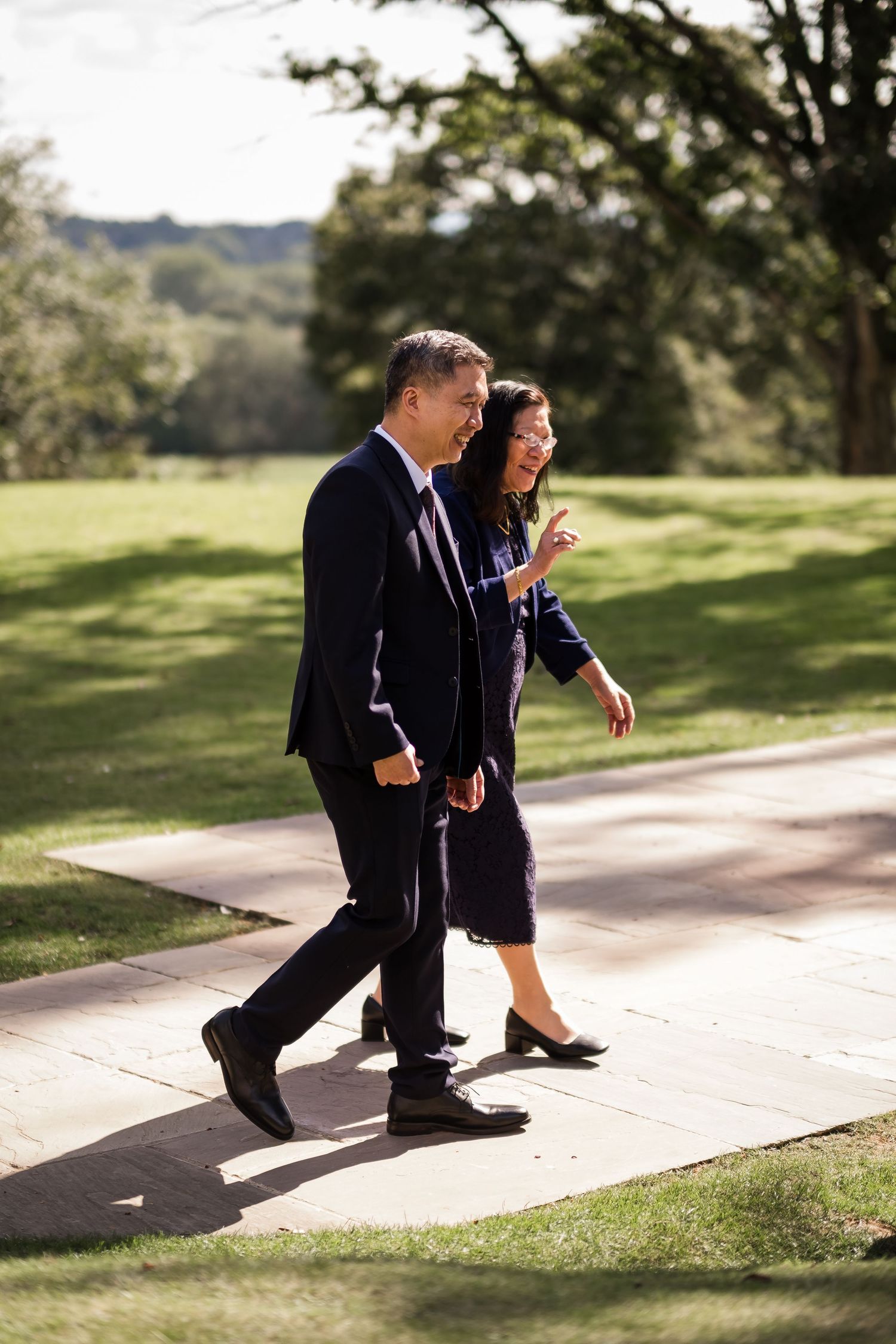 Two people sit together on outdoor concrete steps surrounded by green grass on a sunny day.