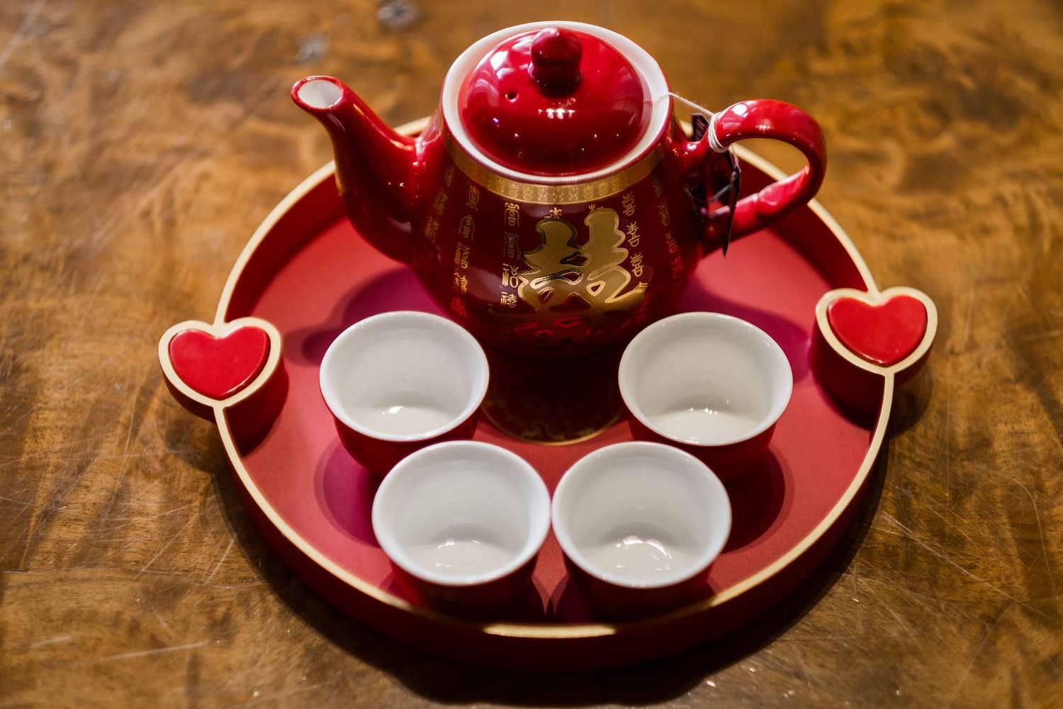 A red heart-shaped ceramic tea set with small white cups arranged on a wooden surface.