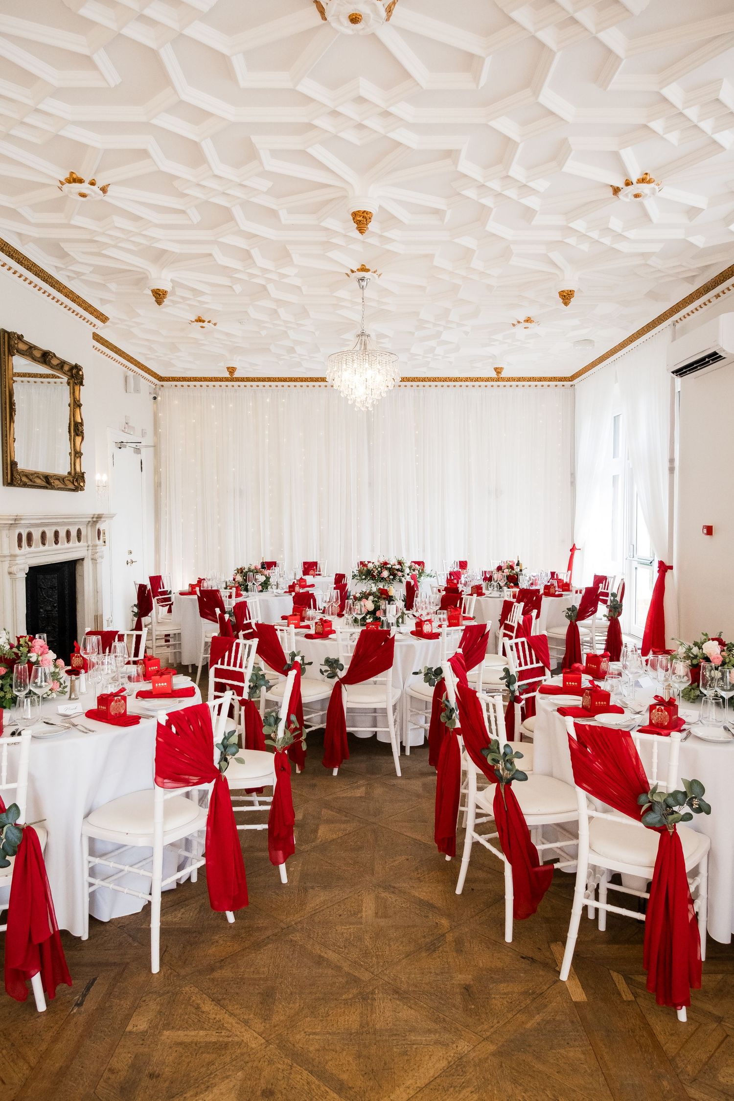 Elegant banquet hall with ornate white ceiling, crystal chandeliers, and tables decorated with red and white linens.