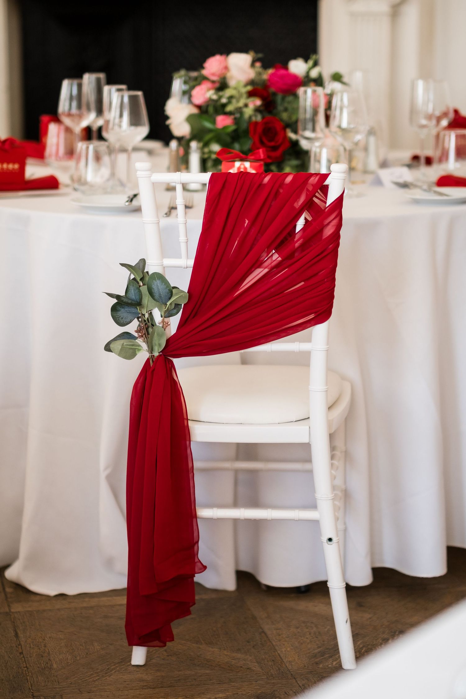Elegant wedding reception table setup with white linens, red napkin decorations, and eucalyptus accents.
