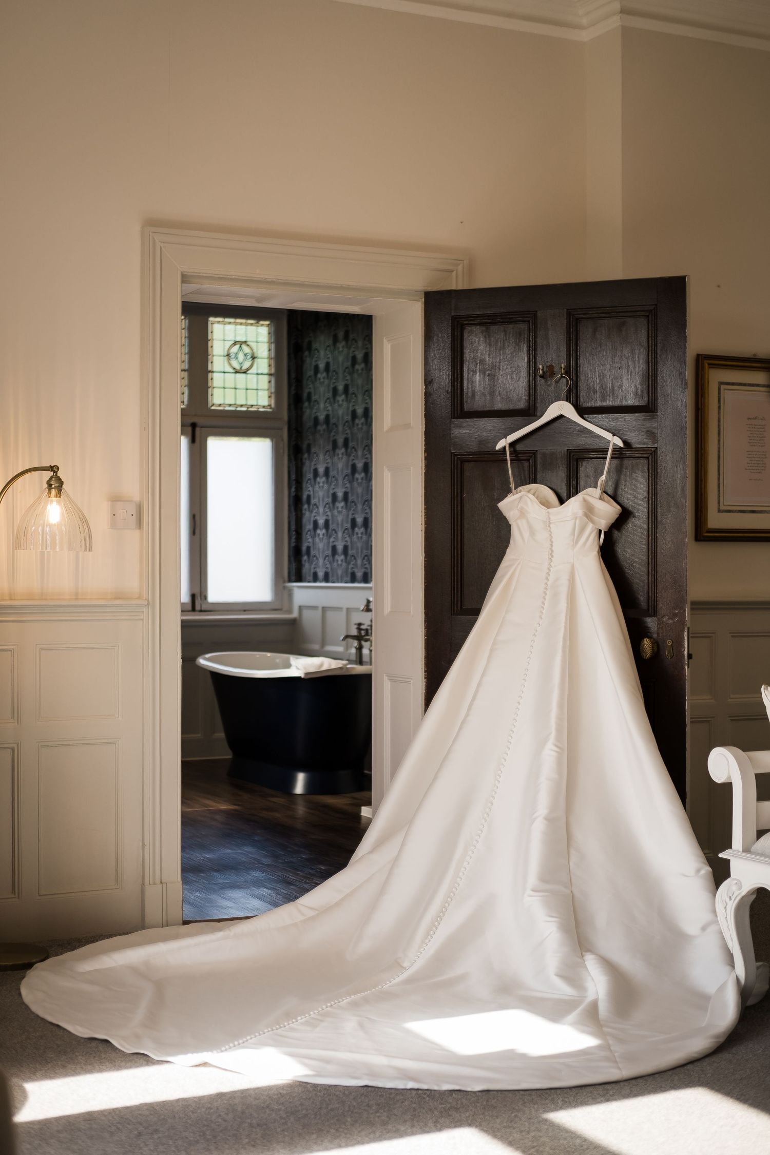 A stunning white wedding dress with a long train displayed in different angles across a sunlit room with dark doors.