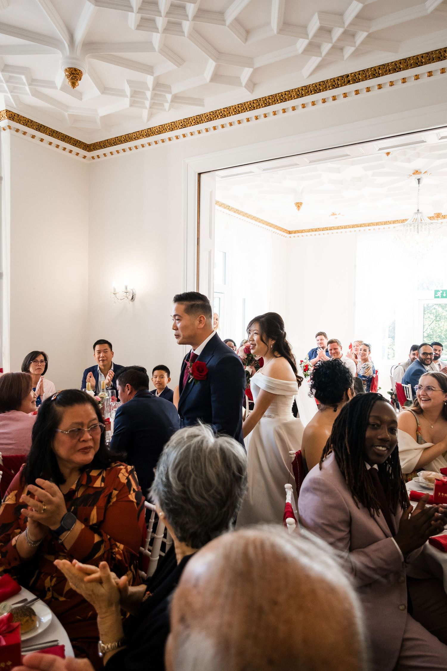A panoramic view of a crowded indoor social gathering with ornate crown molding and decorative ceiling details.