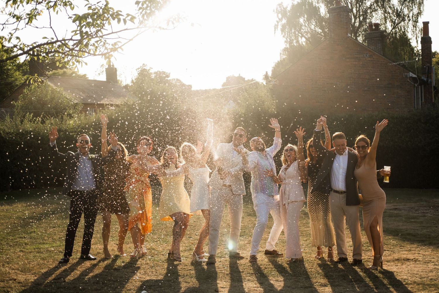 Wedding party stands together in a golden sunlit field during sunset creating a warm and joyful atmosphere.