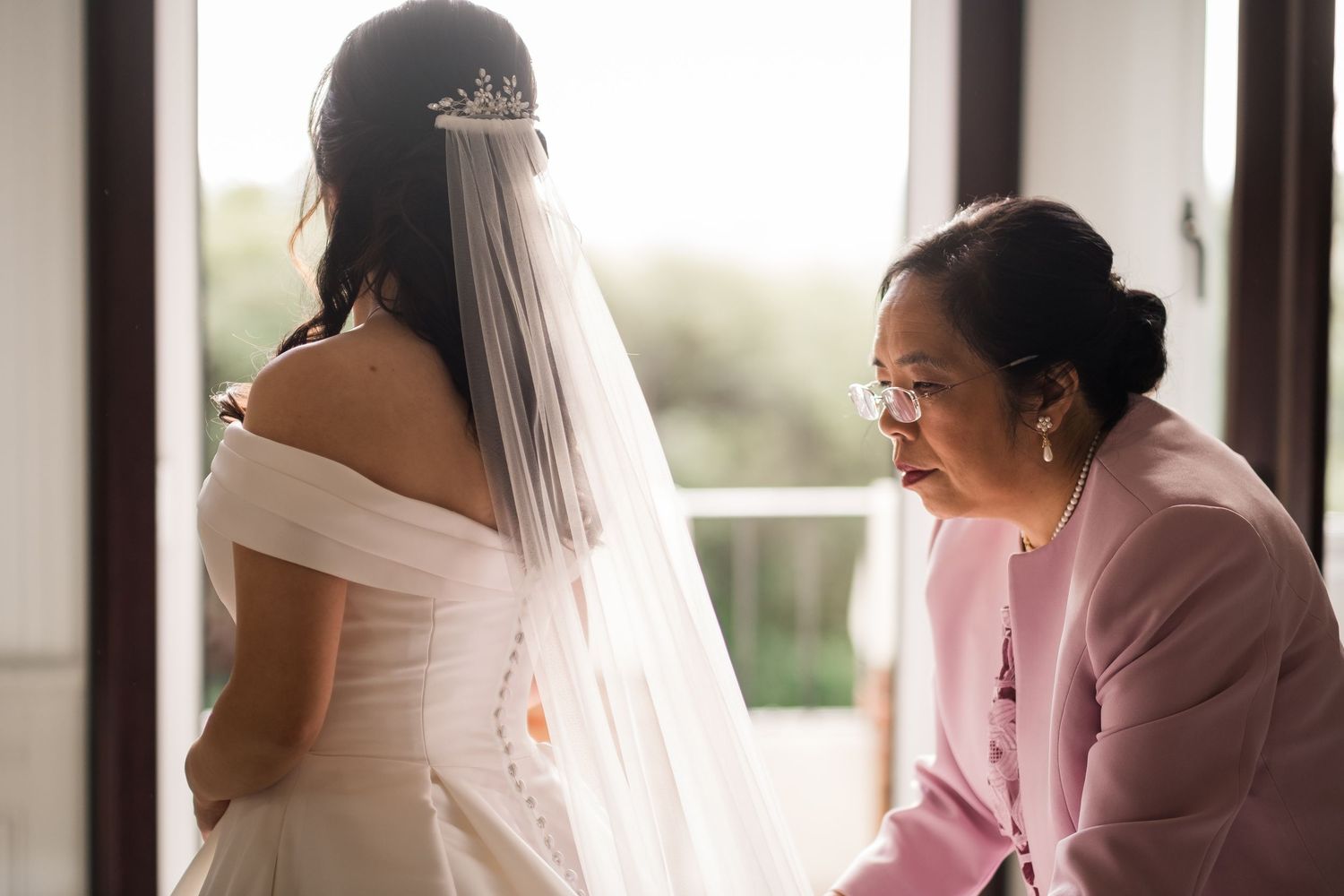 A bride and her bridesmaids in pink dresses share a candid moment while getting ready for the wedding.