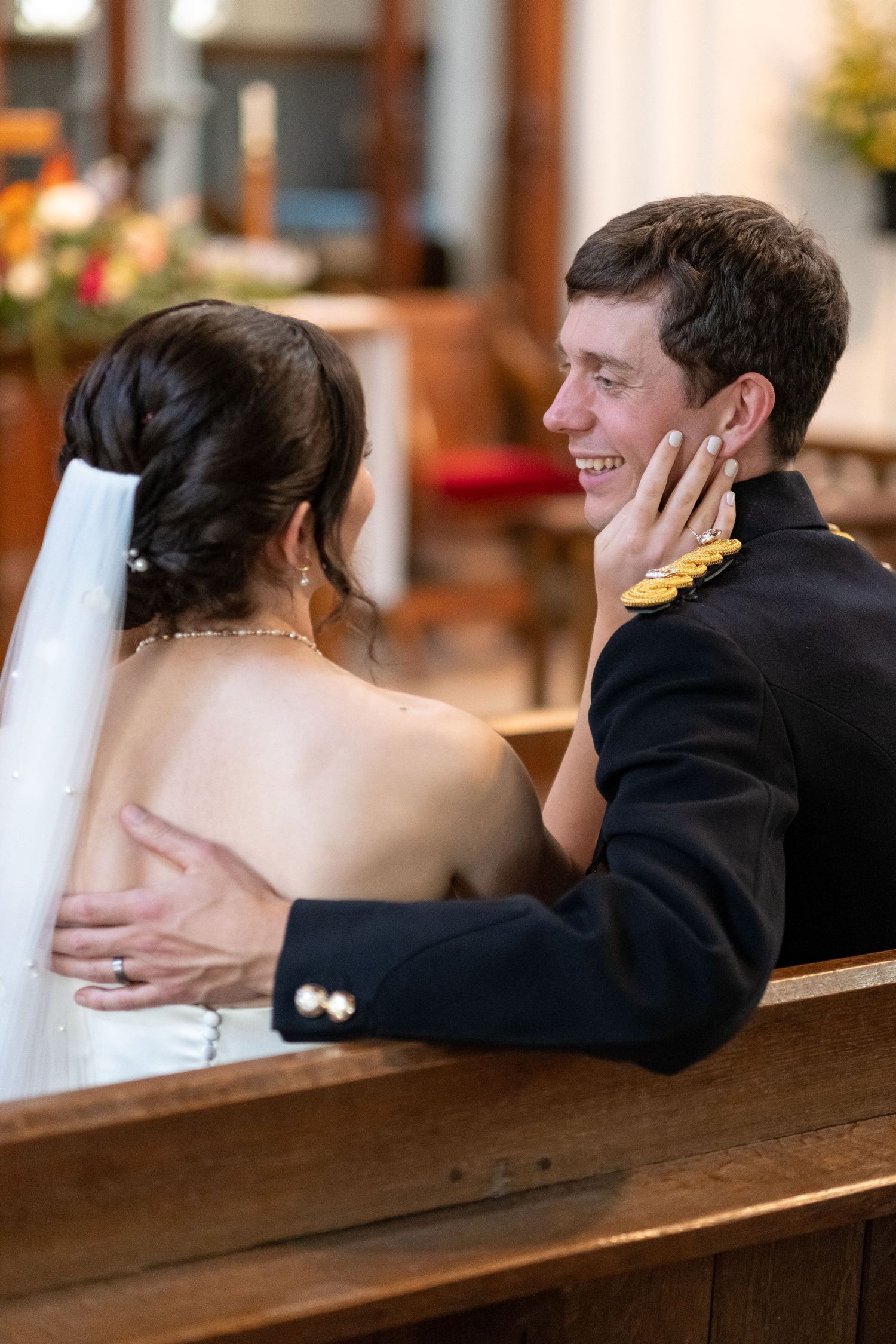 Bride and groom sitting in church pew, bride touching groom's face tenderly during wedding ceremony.