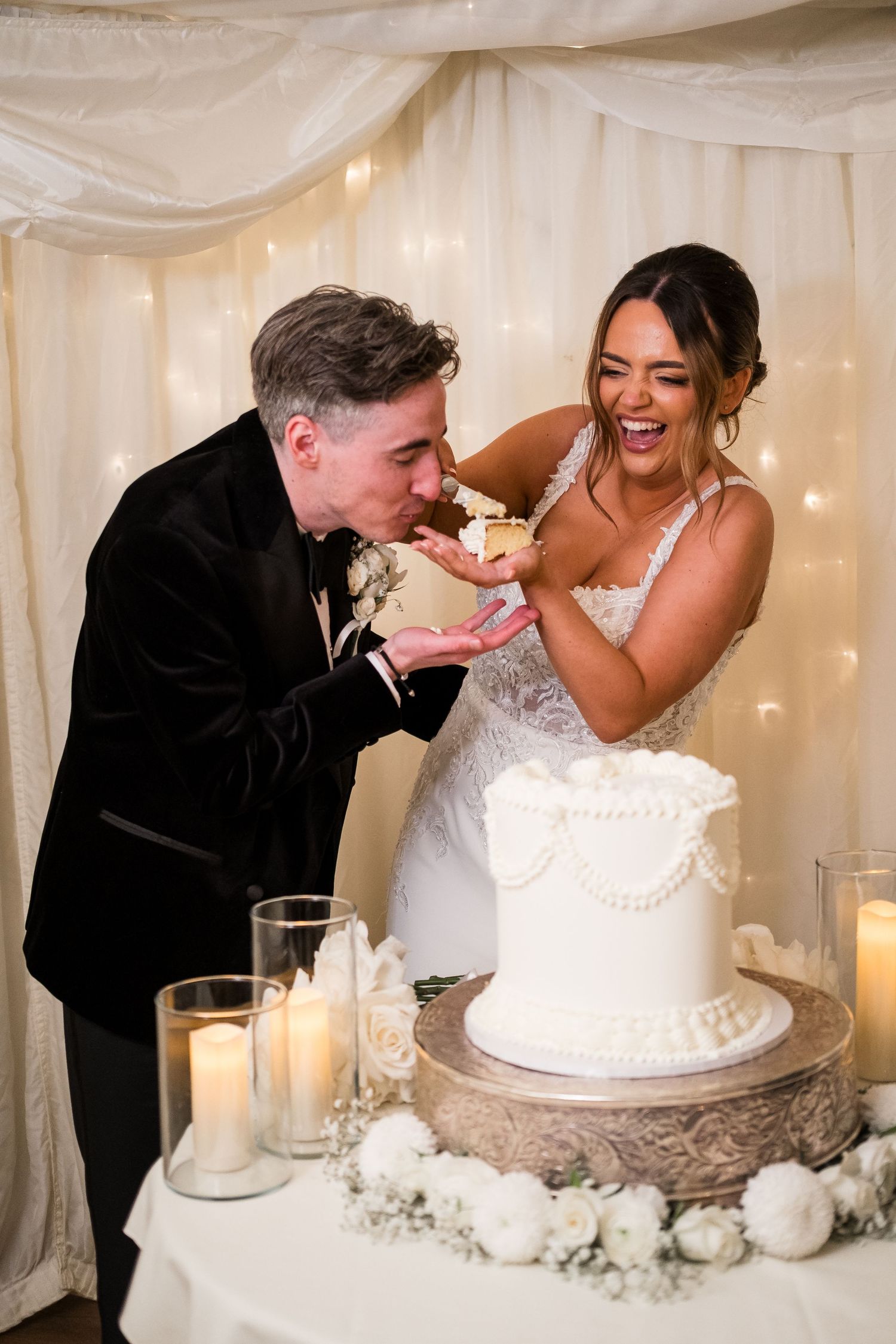 Newlyweds share a playful moment while cutting their elegant white wedding cake at their reception.