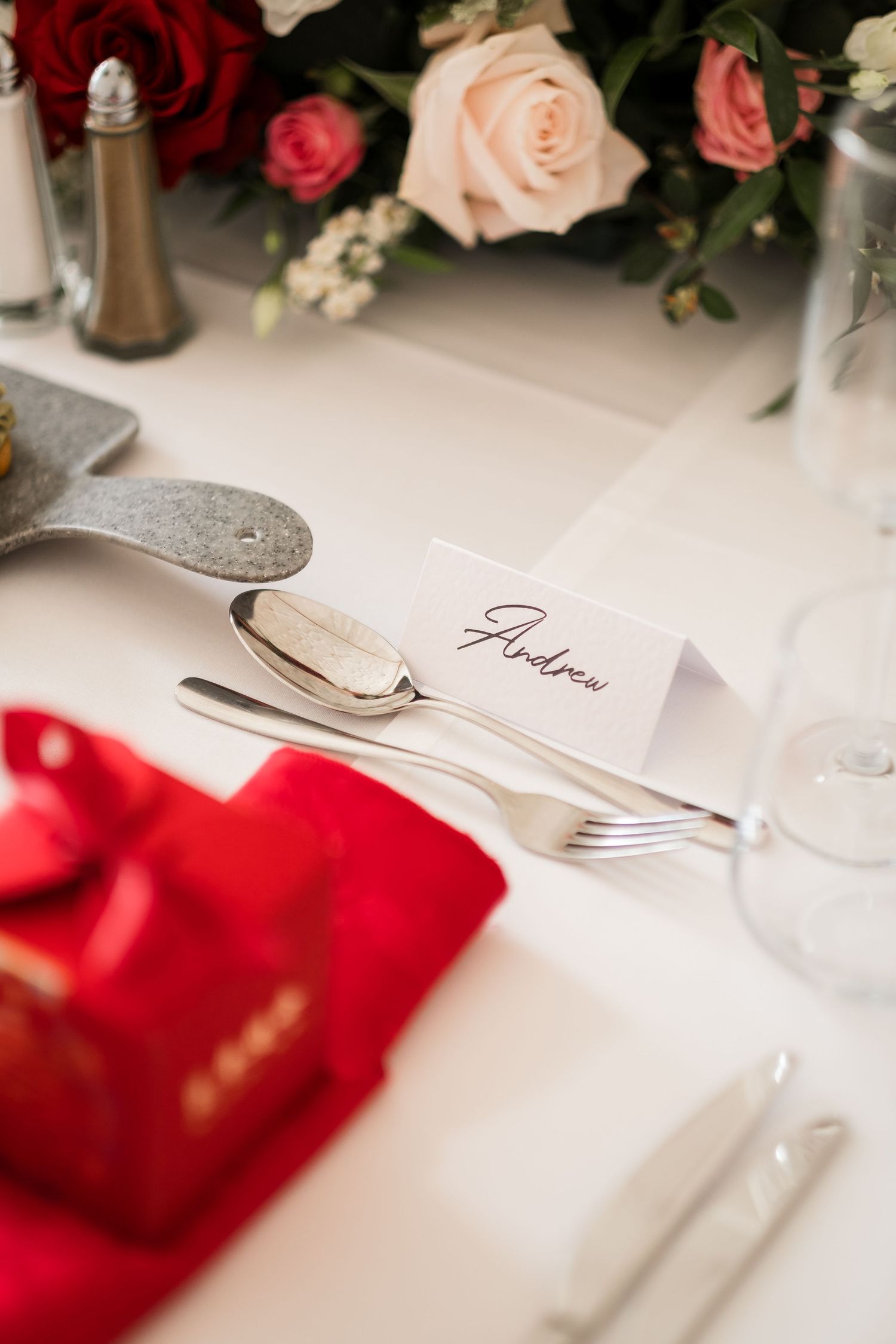 Elegant place setting with red and pink roses, white linens, and silverware at a formal dining table.