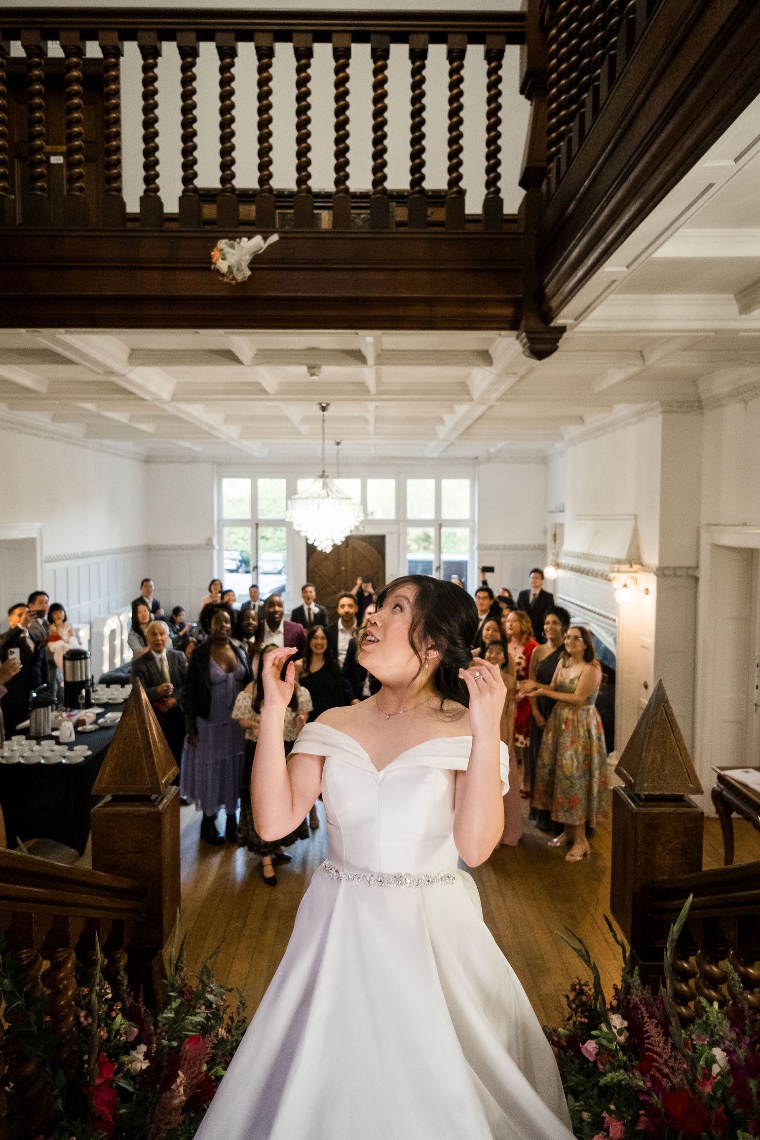 A wedding reception scene in an elegant white room with dark wooden beams and guests gathered around the dance floor.