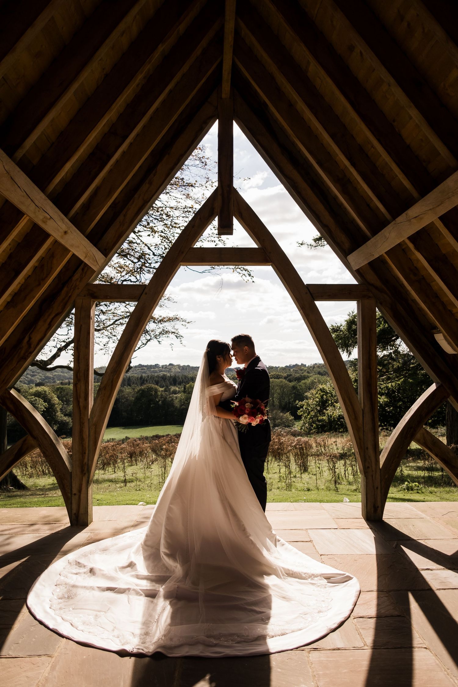 A romantic wedding couple dances in silhouette under a rustic wooden pavilion with dramatic lighting and flowing dress.