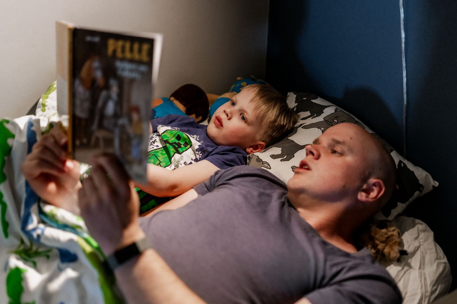 Pappan läser en bok för sonen i sängen.
