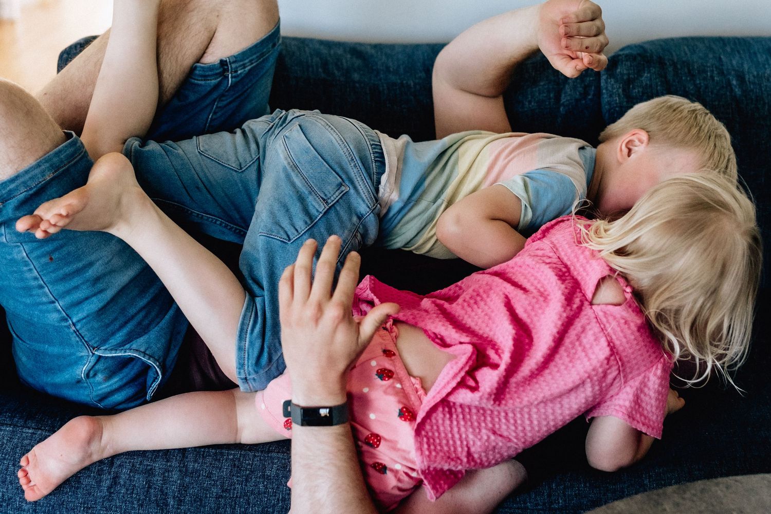 De två barnen hoppar på sin pappa i soffan.