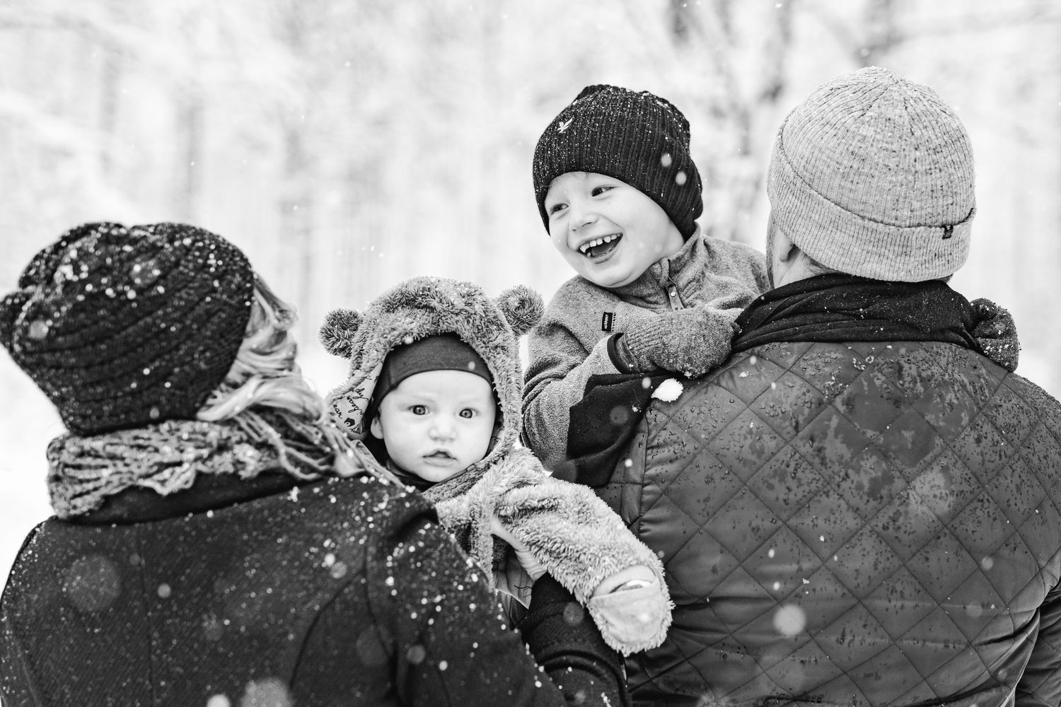De två barnen är i sina föräldrars famn och det snöar runt omkring dem.