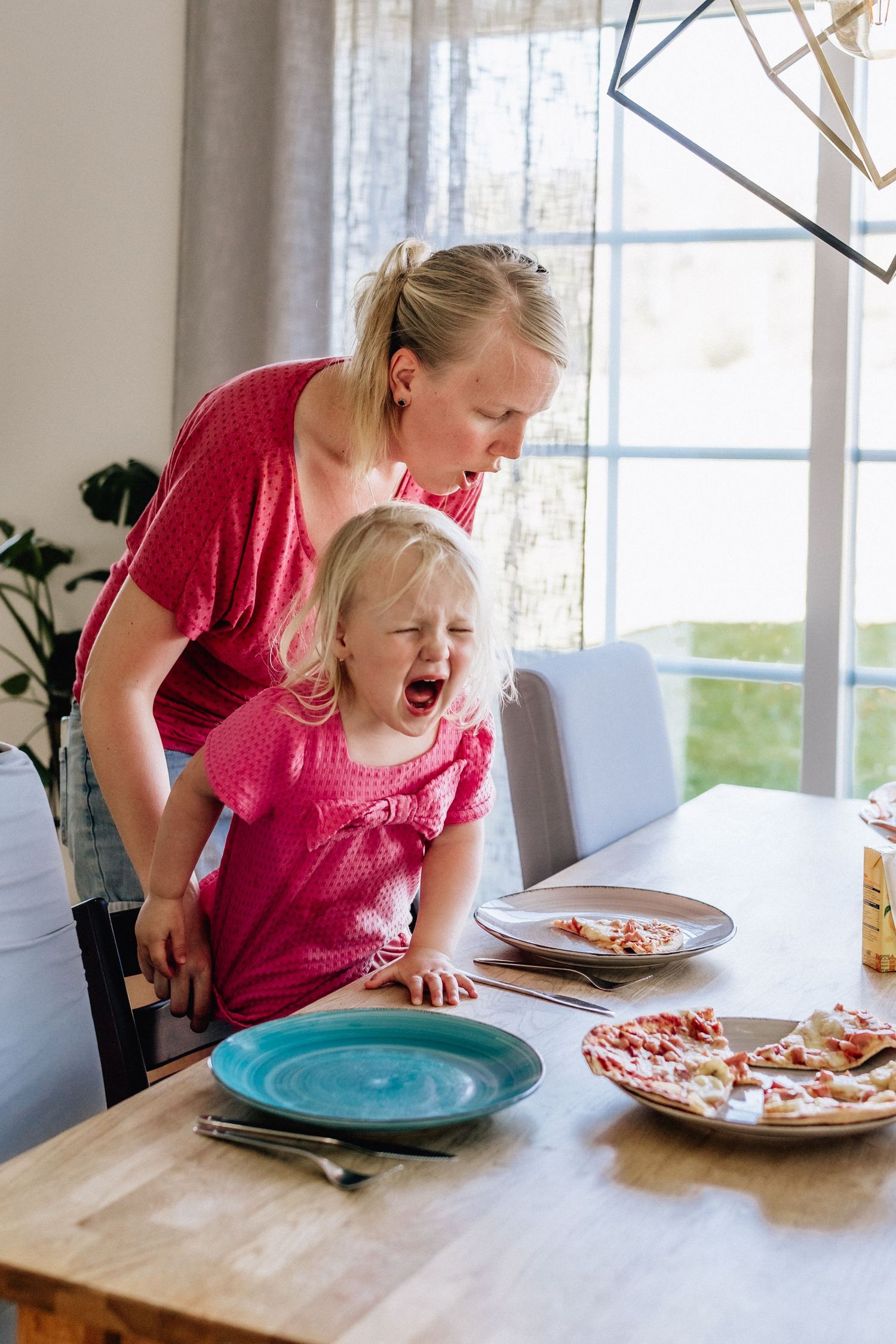 Ett barn skriker vid ett matbord och mamman står bakom.