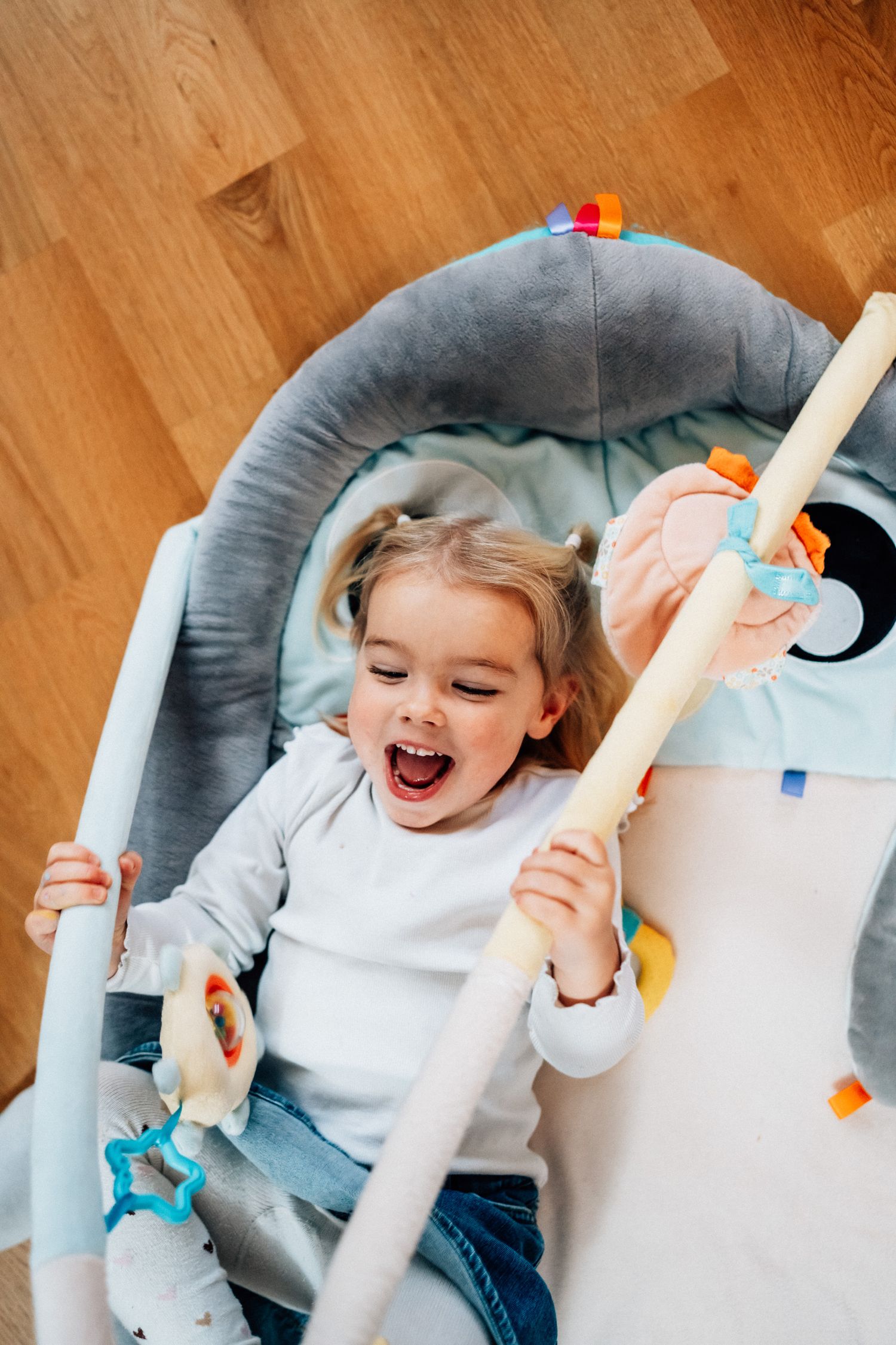 En liten flicka ligger i ett babygym och skrattar under familjefotograferingen.