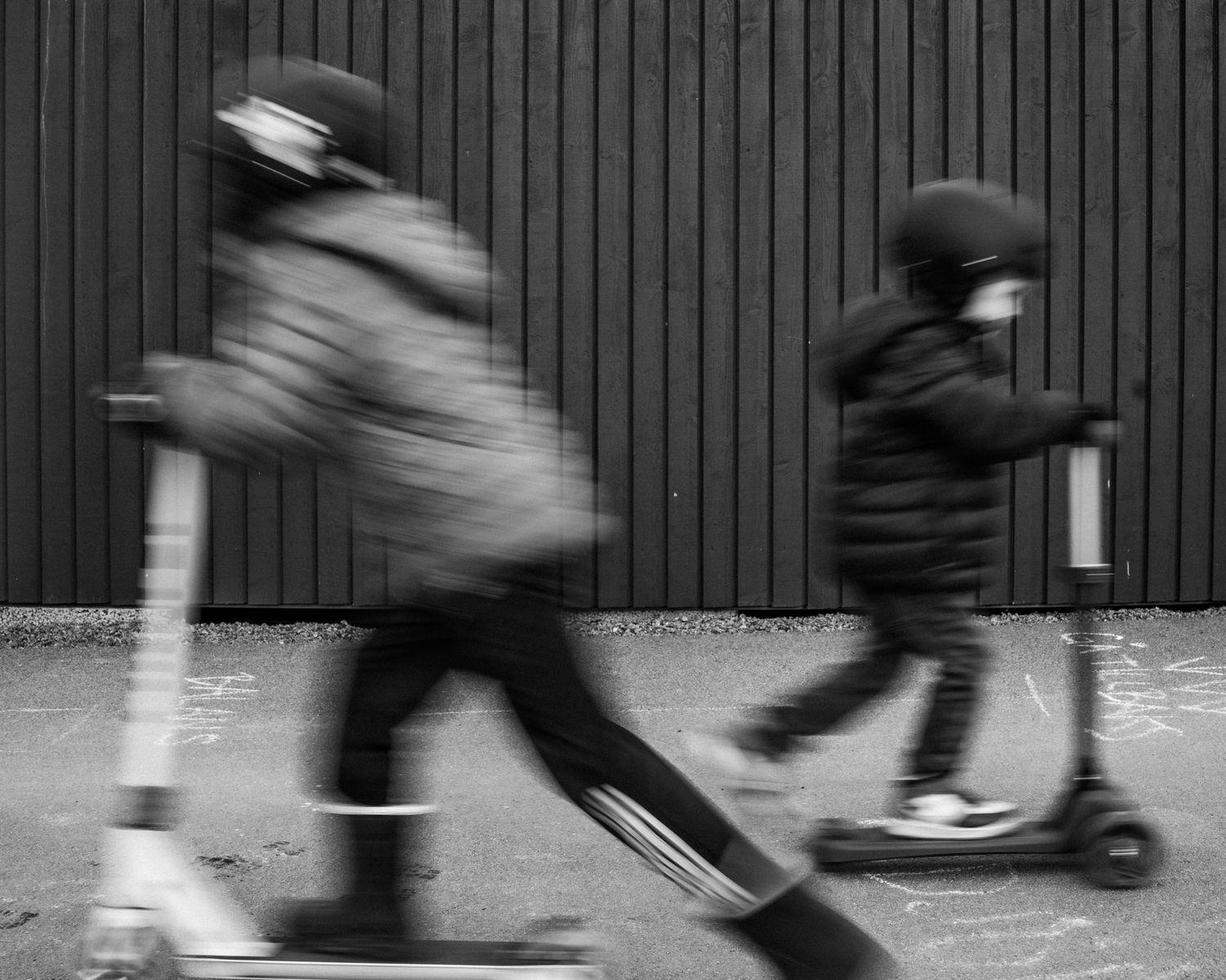 Två barn kör sparkcyklar i motsatt riktning från varandra.