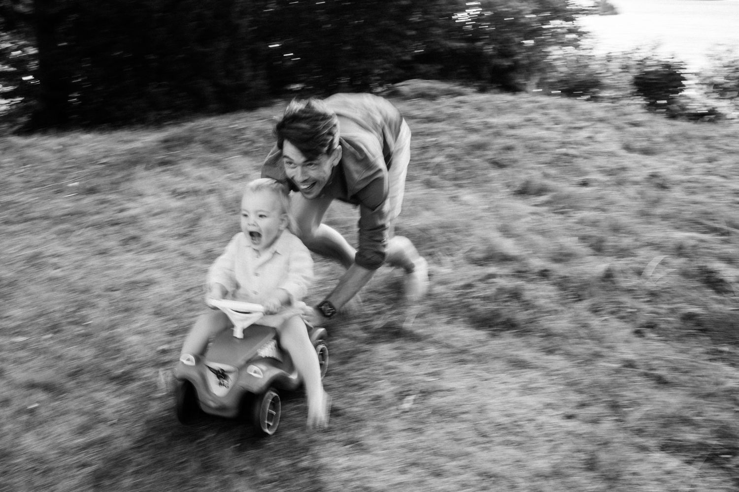 det lilla barnet körs av sin pappa på sin bobby car.