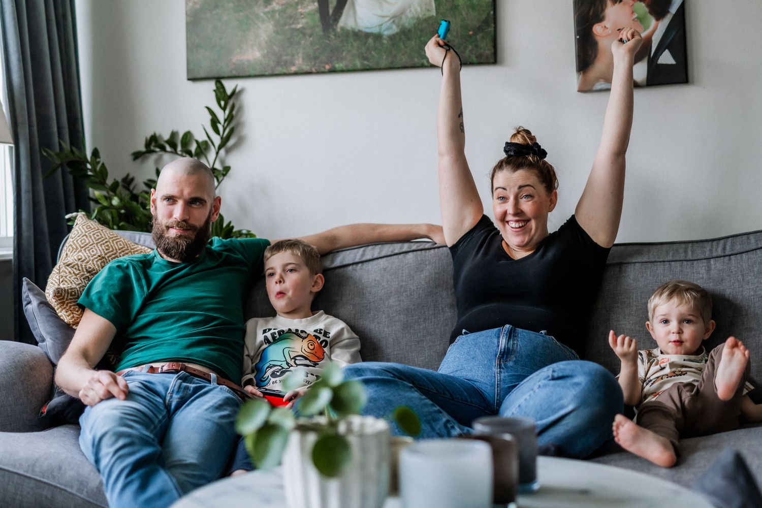 Familjen sitter i soffan och mamman gör en segergest med en Tv-spelskontroll i handen.