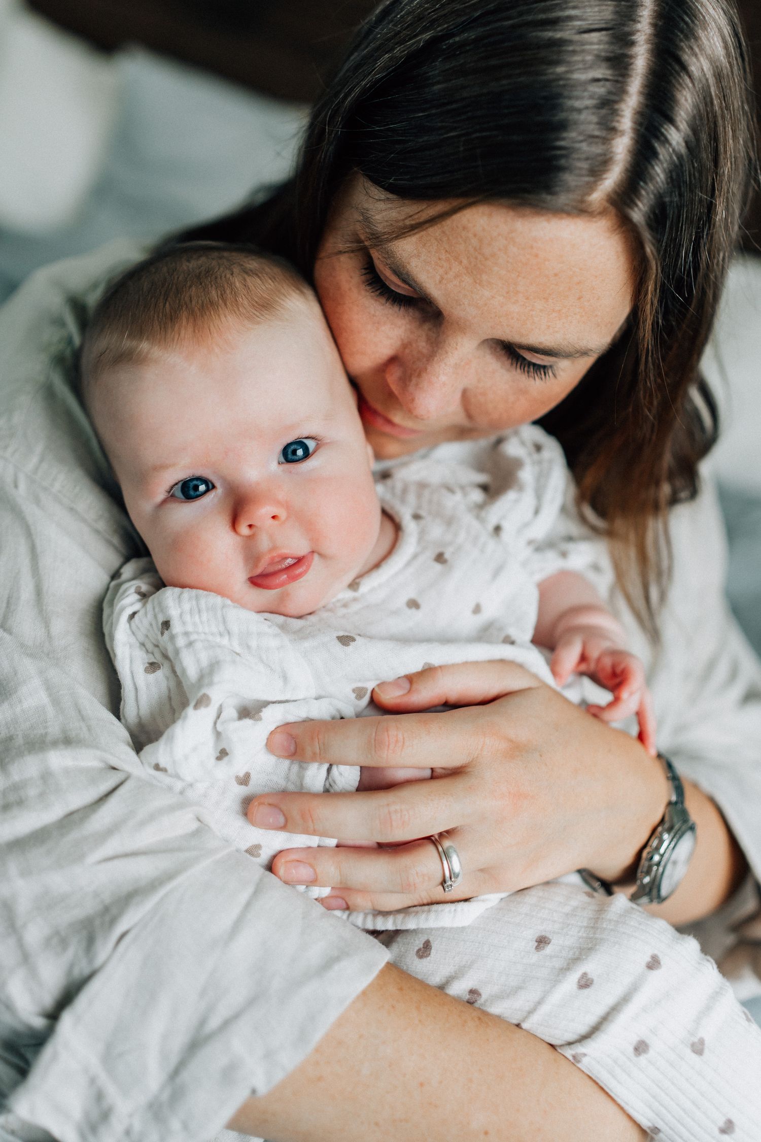 Bebisen i sin mammas famn tittar in i kameran under bebisfotograferingen.