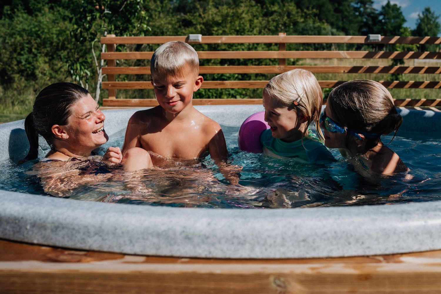 En familj med tre barn sitter i en pool en solig sommardag under den dokumentära familjefotograferingen i Linköping.