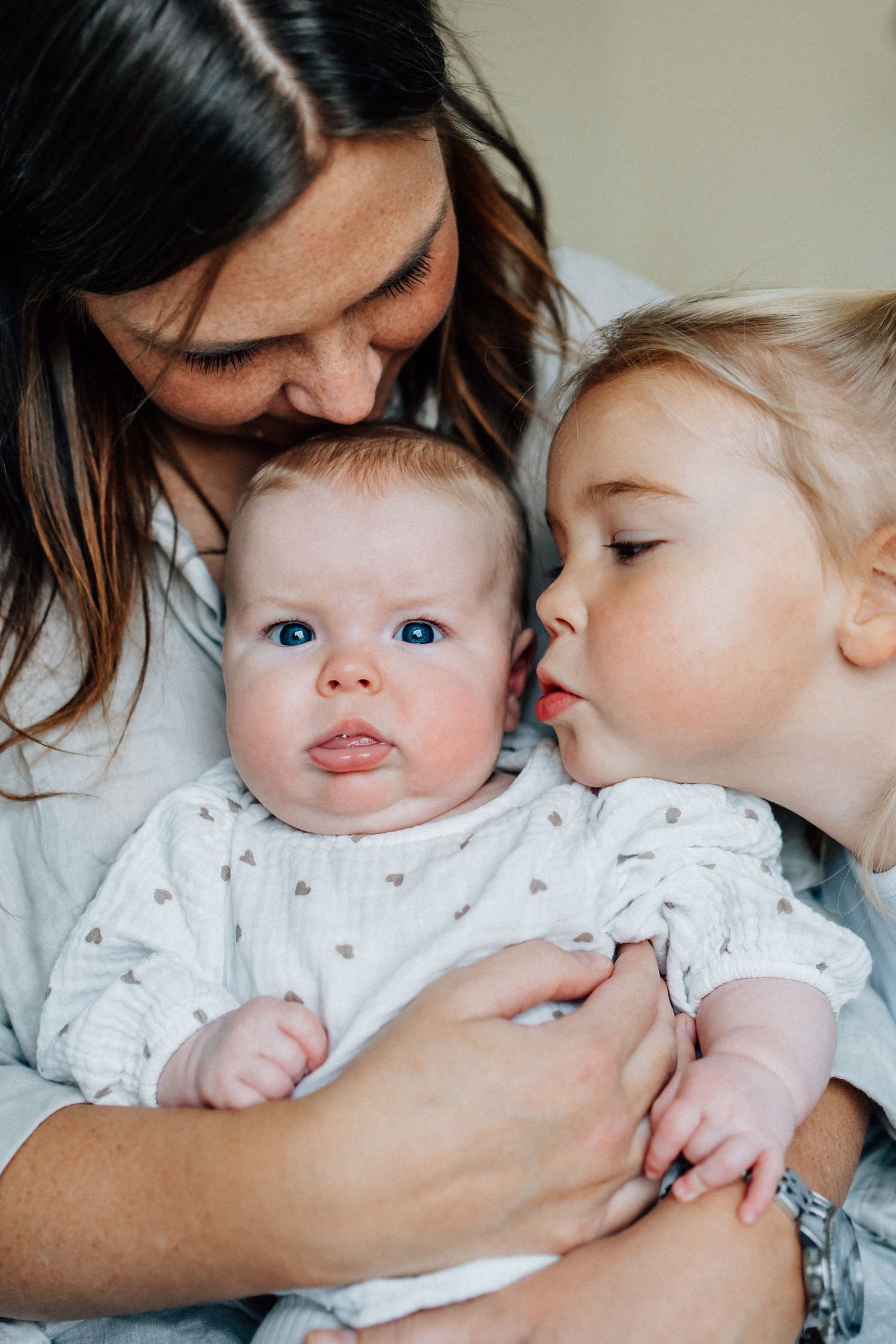 En mamma och en storasyster pussar på en liten bebis.