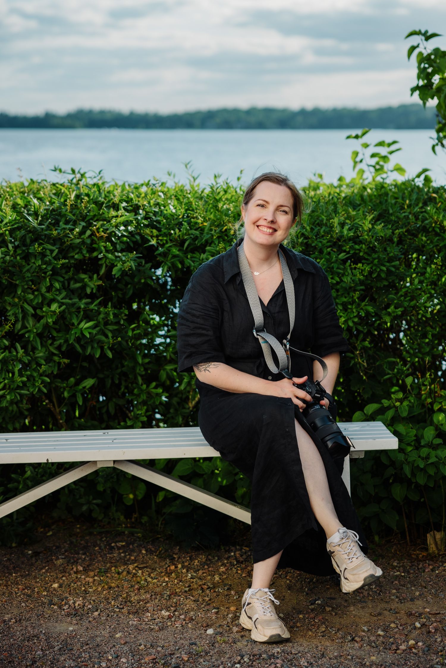 Fotograf Jenny Widén sitter på en bänk vid en sjö och ler.