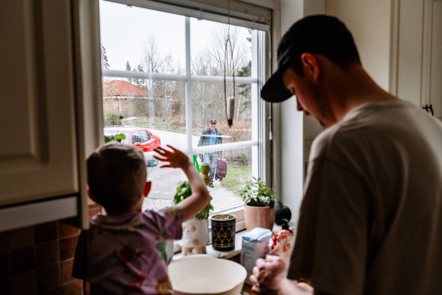 Barnet och pappan står vid ett fönster och vinkar till någon utanför.