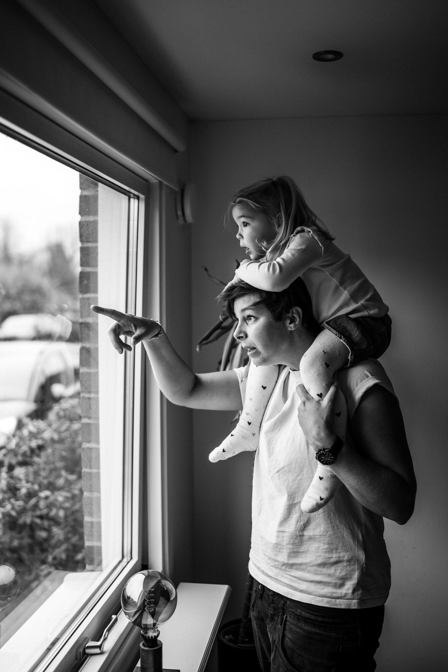 Barnet sitter på sin mammas axlar och de tittar ut genom fönstret.