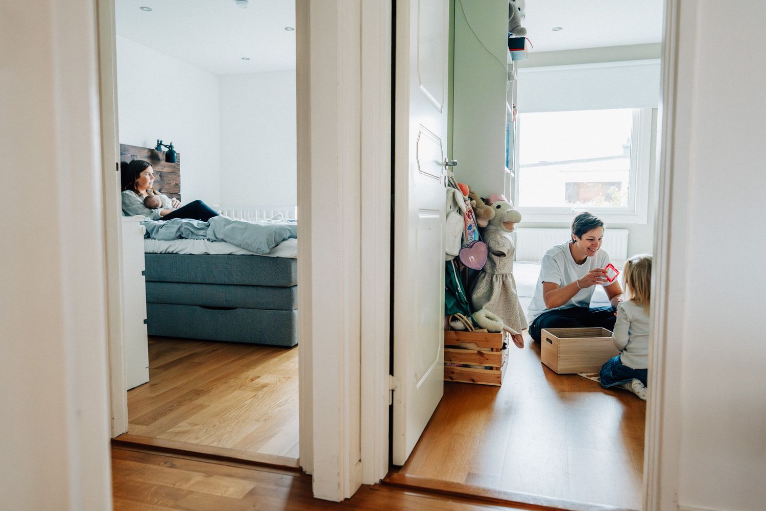 Två rum syns i bilden – i ett sitter en mamma och ammar en bebis och i det andra sitter en mamma och leker med sin dotter.