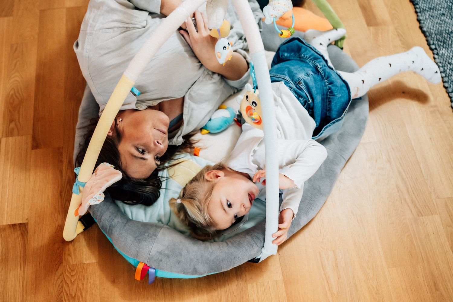 En mamma ligger bredvid sin dotter på ett babygym på golvet.