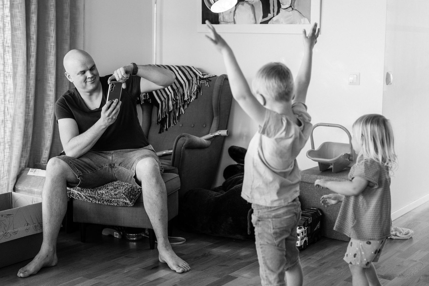 Pappan fotograferar sina två barn med mobilen.