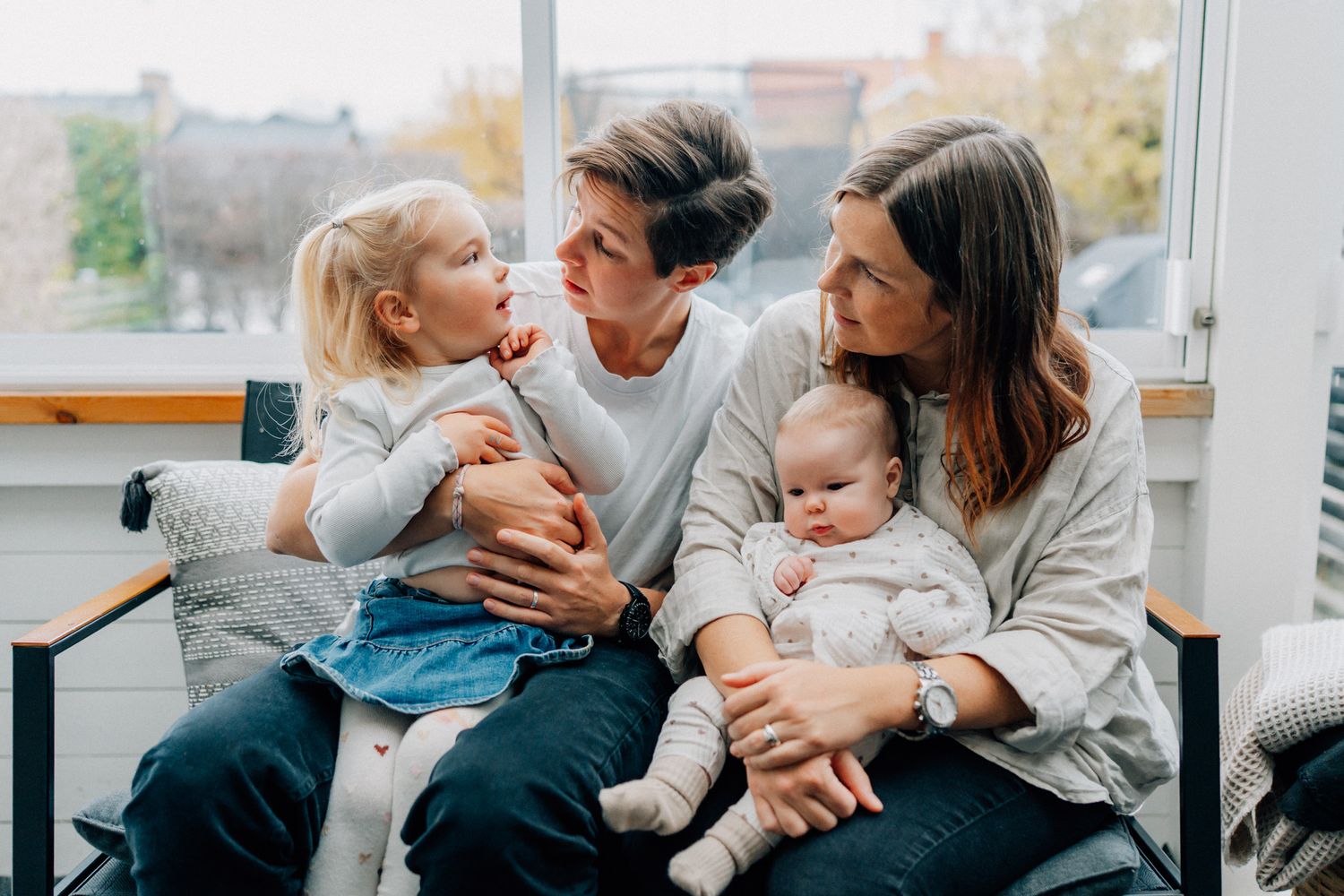 En familj sitter tillsammans på en soffa i ett uterum och tittar på storasyster.