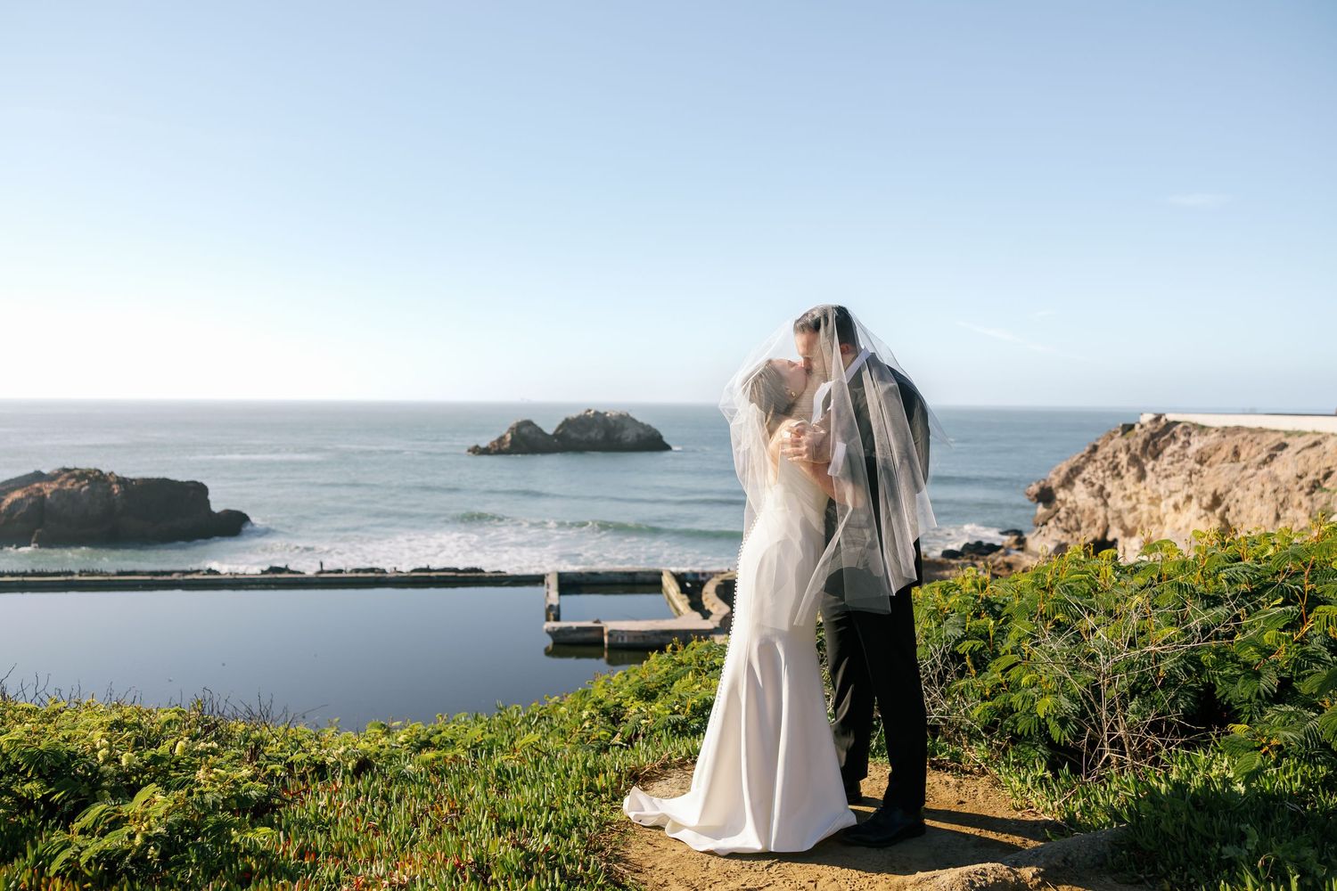 Coastal landscape view with someone standing on a cliff overlooking the Pacific Ocean and rocky islands on a sunny day.