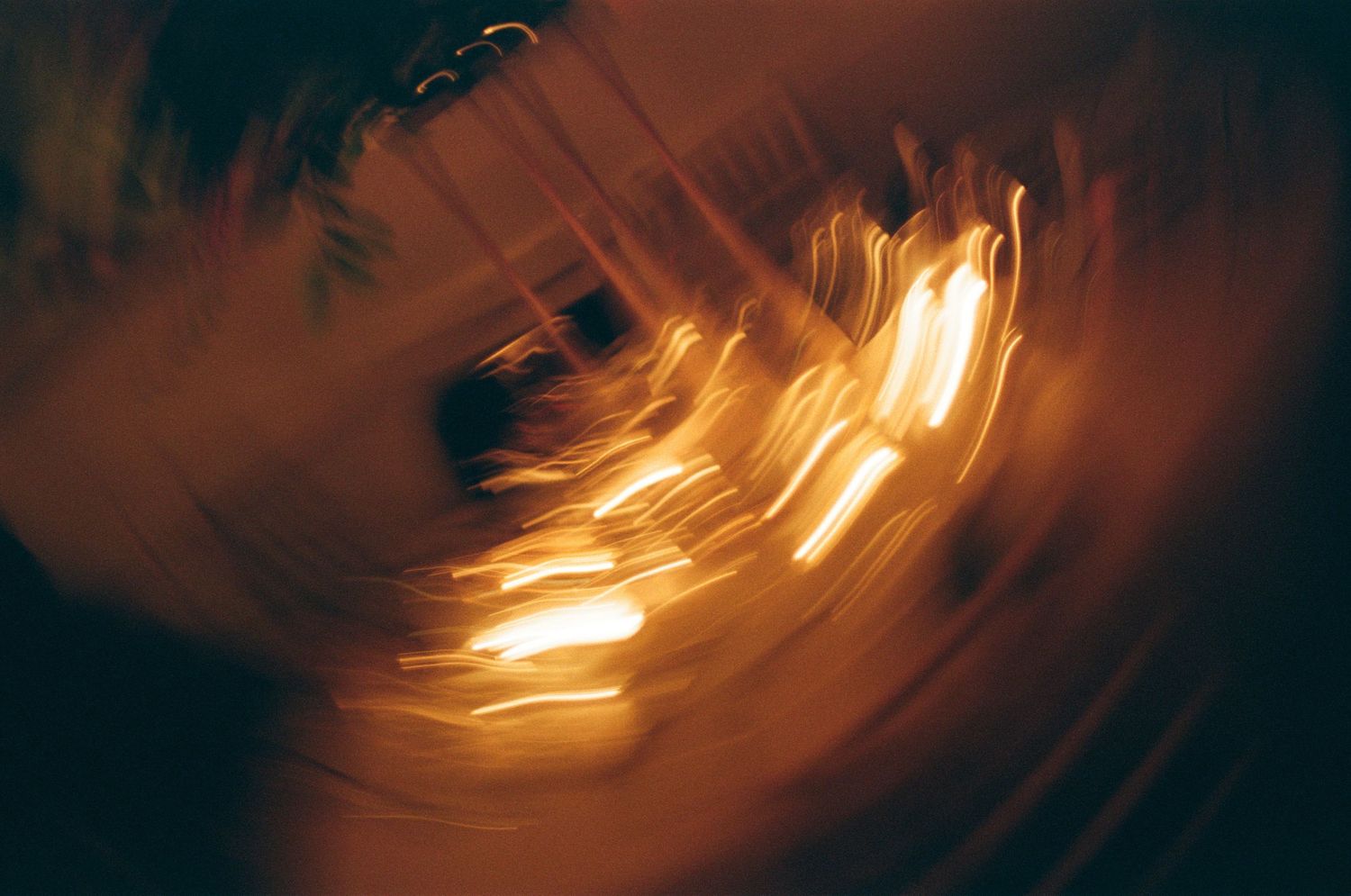 Blurred golden light streaks from candles create an ethereal pattern in darkness on 35mm film photo in Savannah, GA.