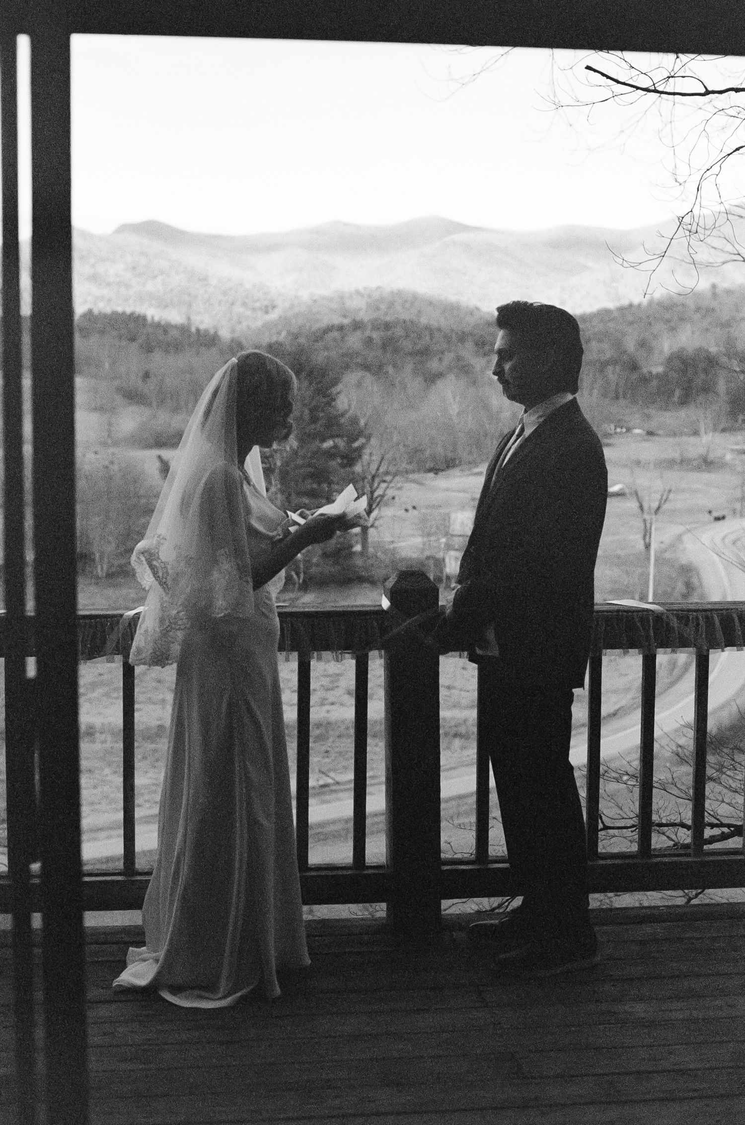 Black and white photo of a bride and groom exchanging vows on a mountain deck with scenic valley views.