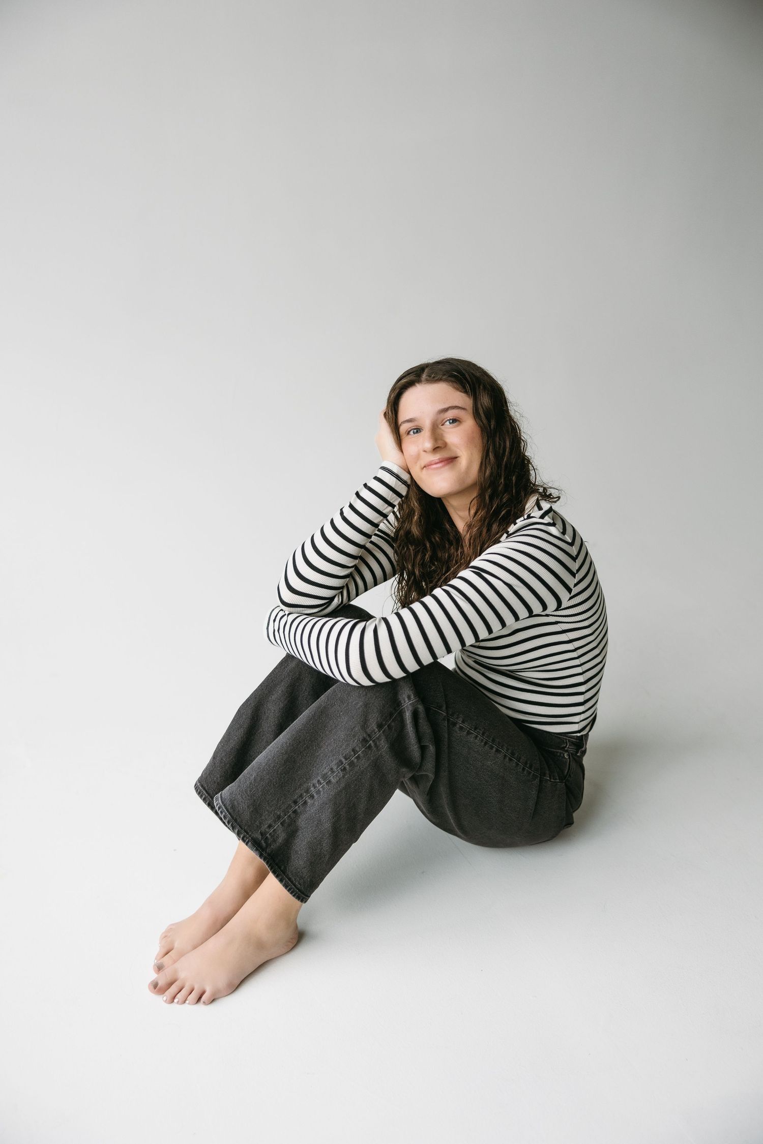 Woman in striped shirt sitting casually against white backdrop.