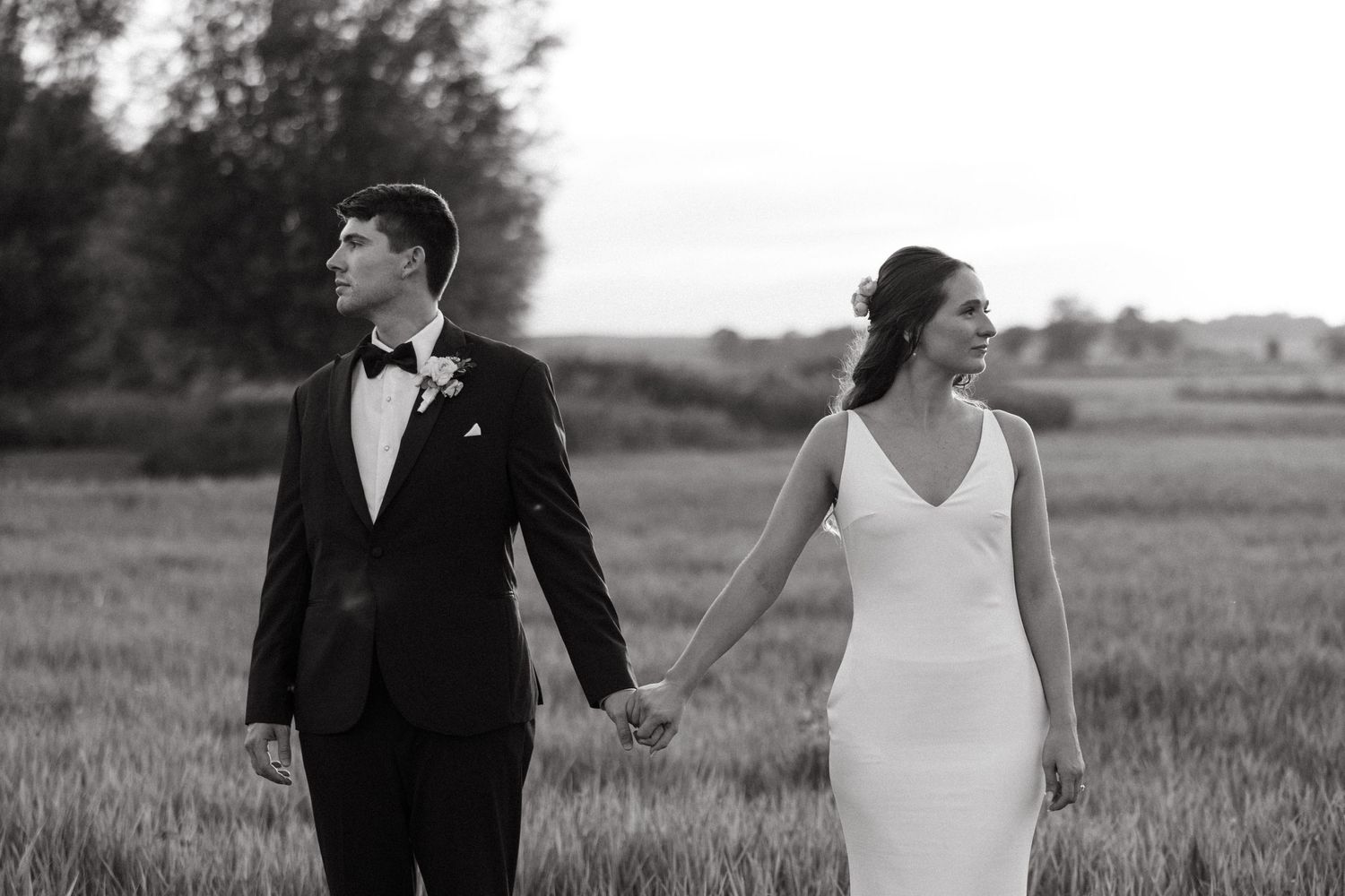 Black and white portrait of newlyweds walking together in a rustic field.