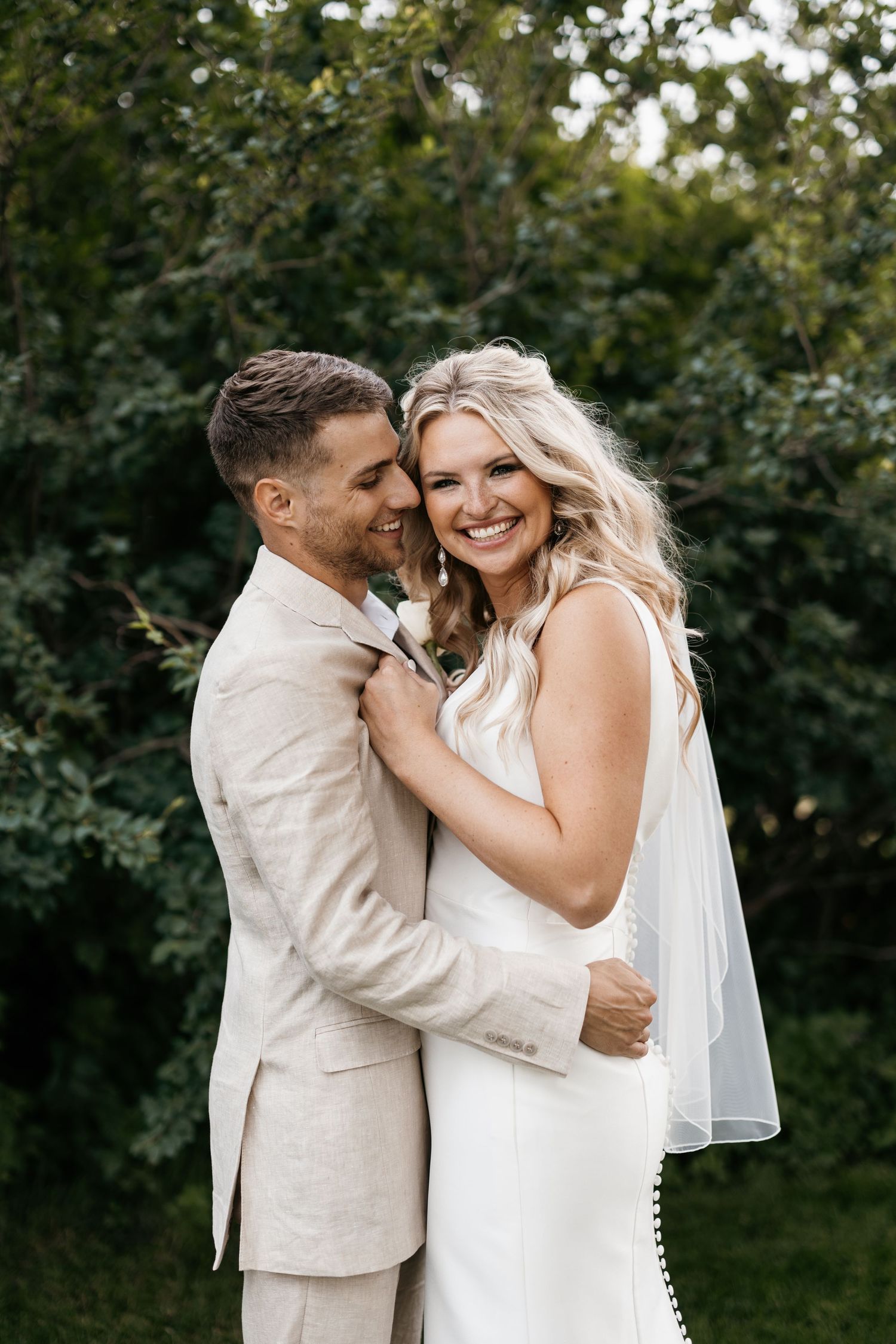 Joyful wedding couple embracing outdoors against lush green foliage backdrop.