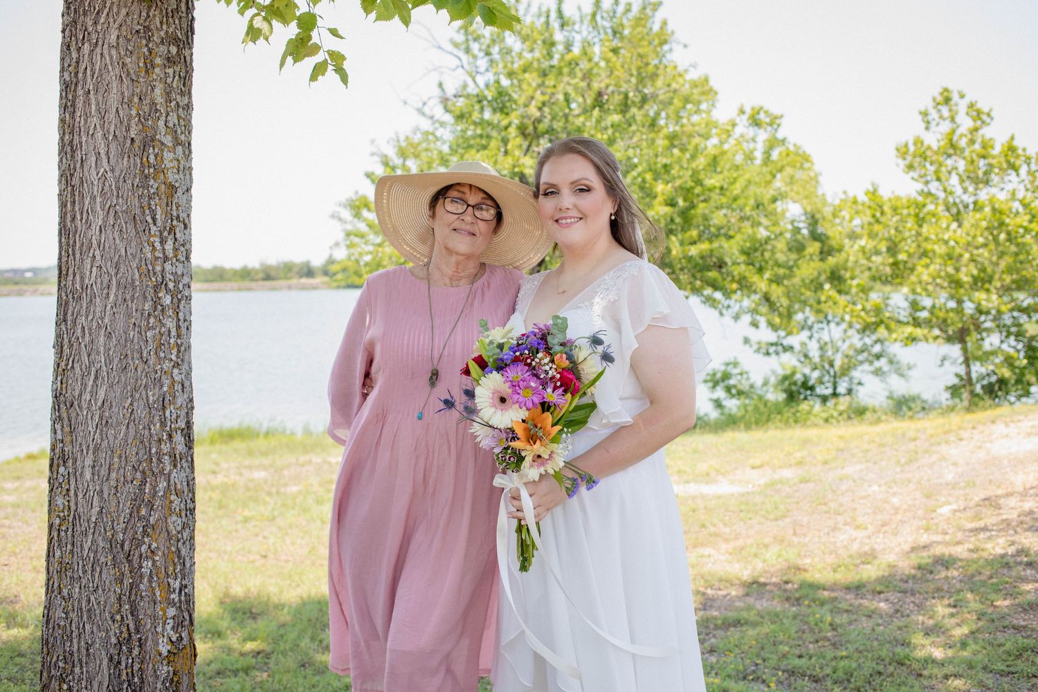 Wedding portrait of two people standing by a lake with colorful bouquet and pink dress.