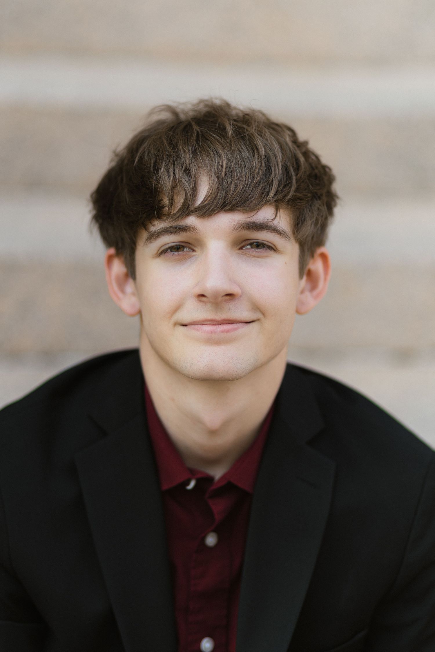 Person wearing a black blazer and burgundy polo shirt smiles warmly at the camera.
