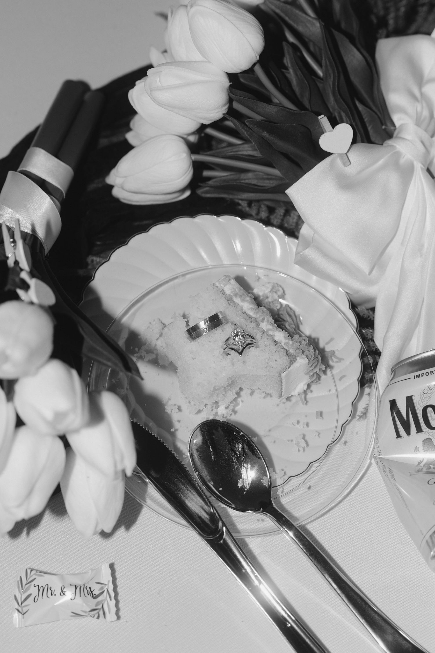 Black and white flat lay of wedding items including flowers, a spoon, cosmetics, and decorative accessories.