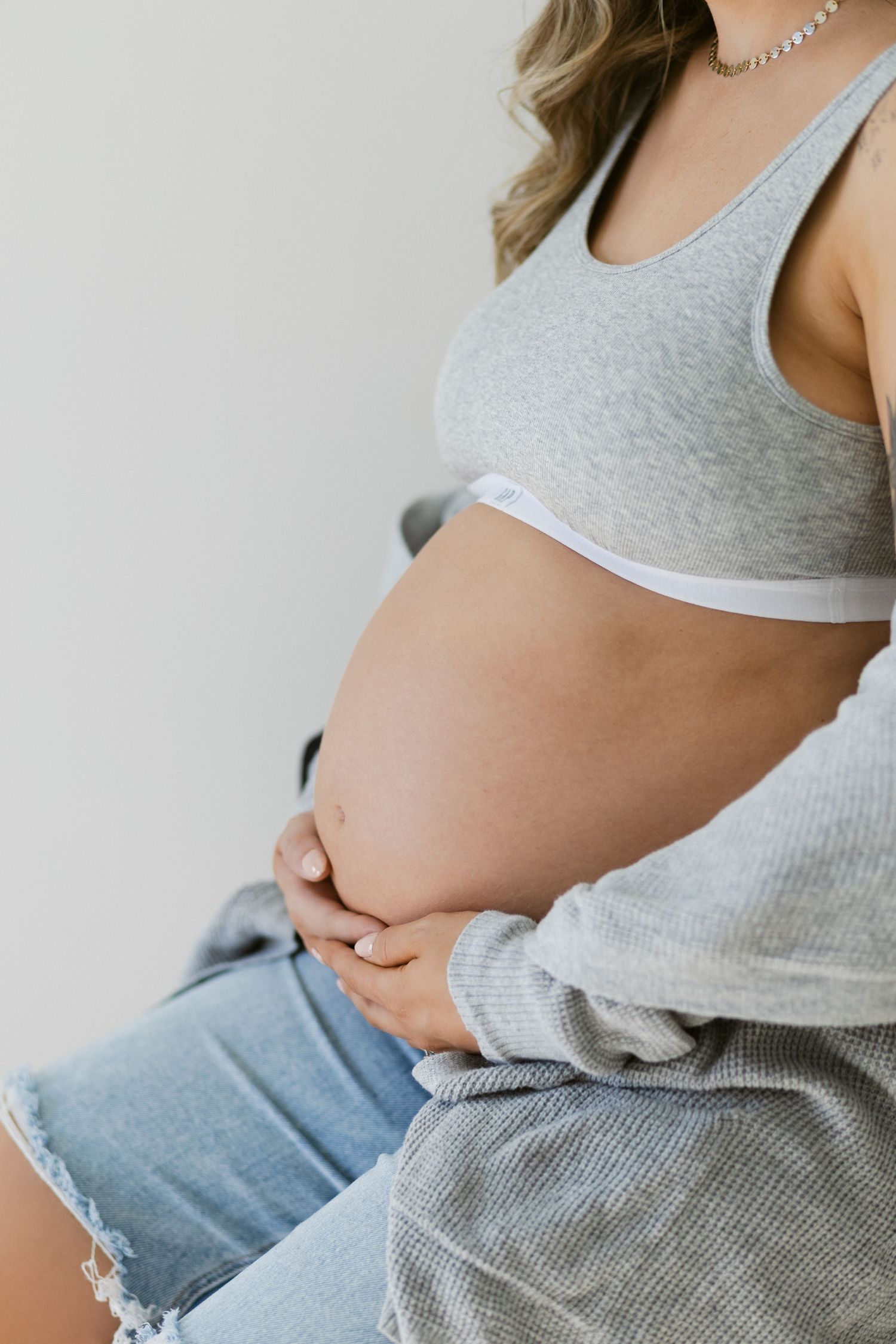 Pregnancy progression shown in four connected photos of a growing baby bump with grey top and jeans.