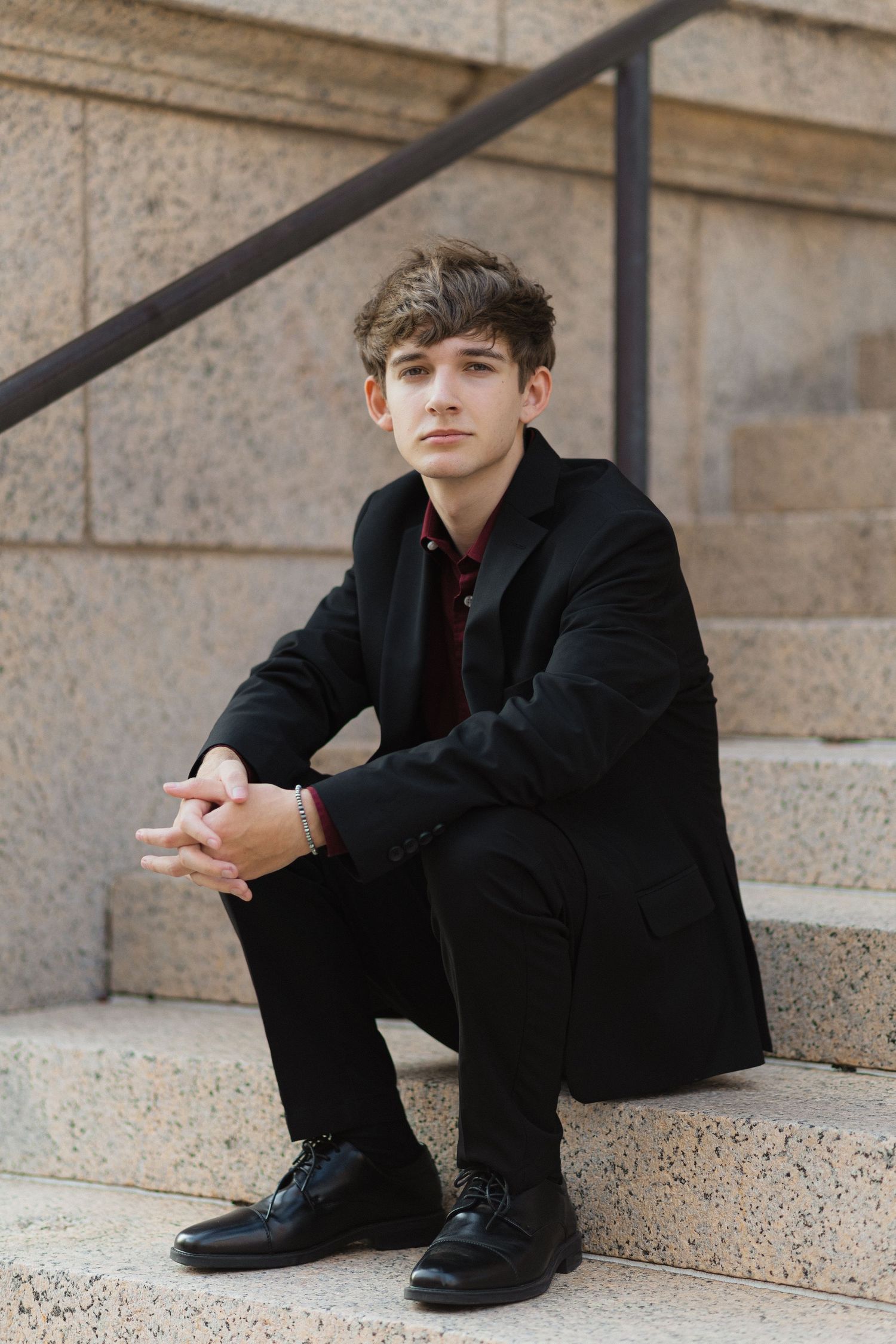 Person in black suit sitting thoughtfully on concrete steps near a railing.