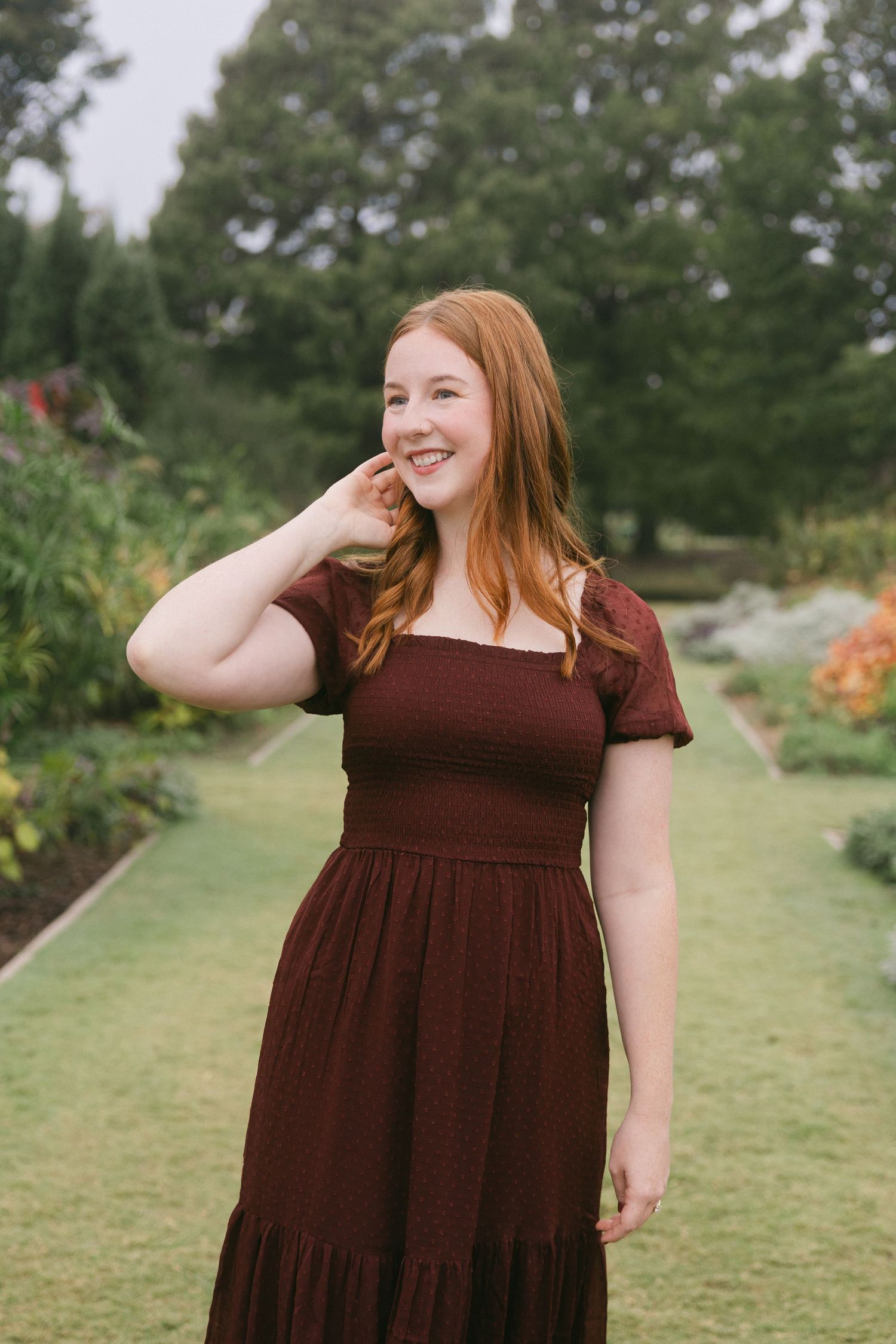 A person in a brown dress stands in a lush garden setting, shown in a series of candid poses.