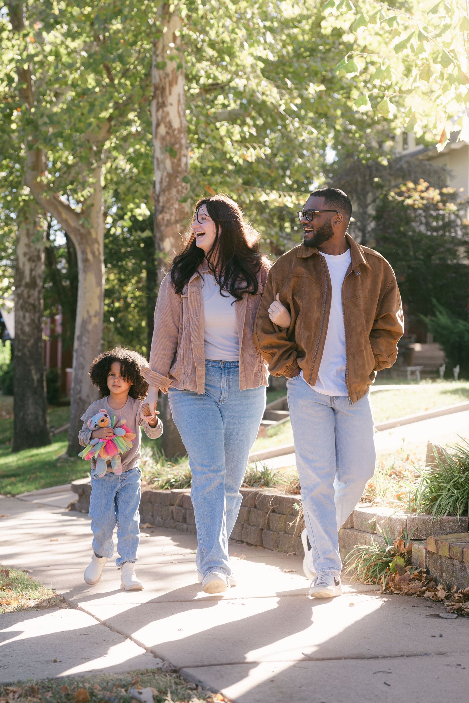 A group walks together along a sunlit stone path wearing matching denim and brown jackets on an autumn day.