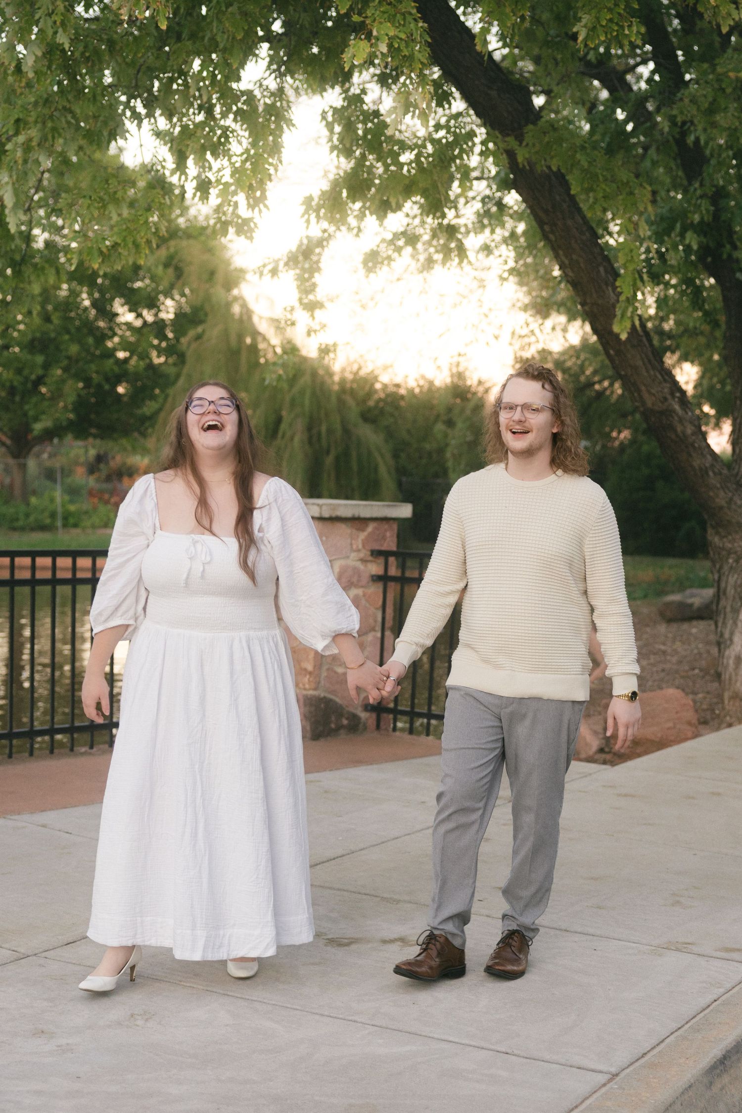 A couple in white and gray attire share joyful candid moments together on a stone patio during a sunset photoshoot.