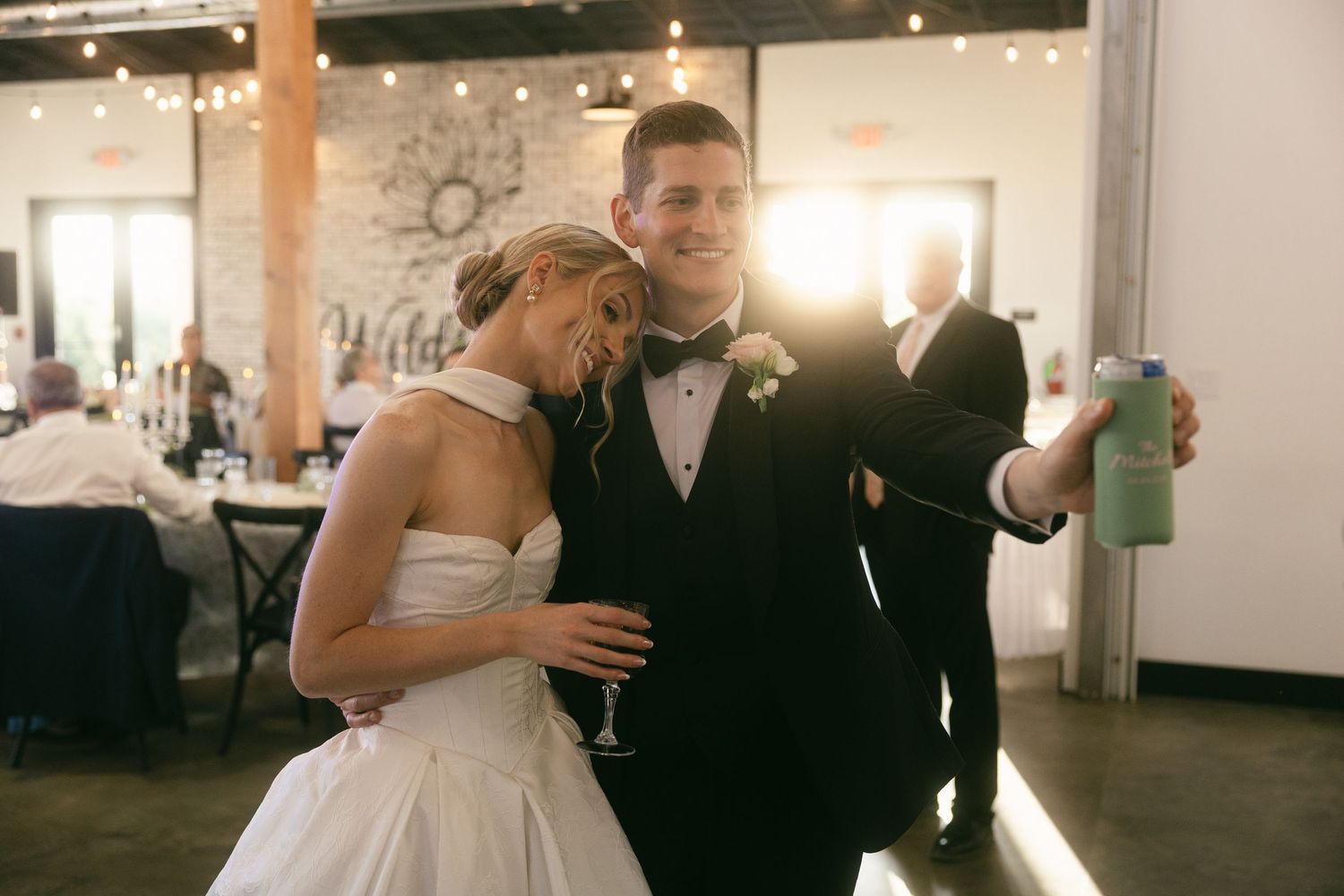 Bride and groom take a selfie together at their wedding reception in an elegant venue with string lights.