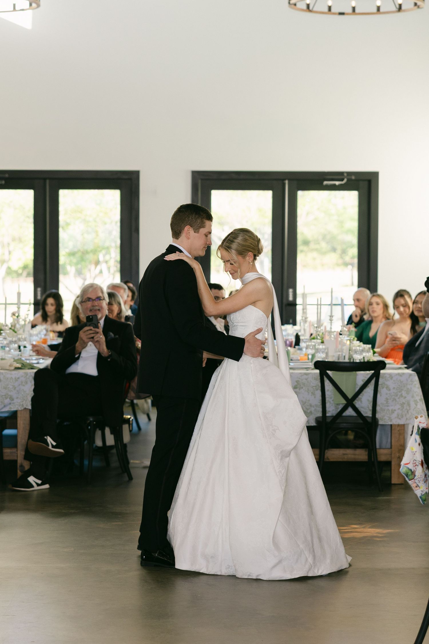 Bride and groom sharing first dance at wedding reception while guests watch.