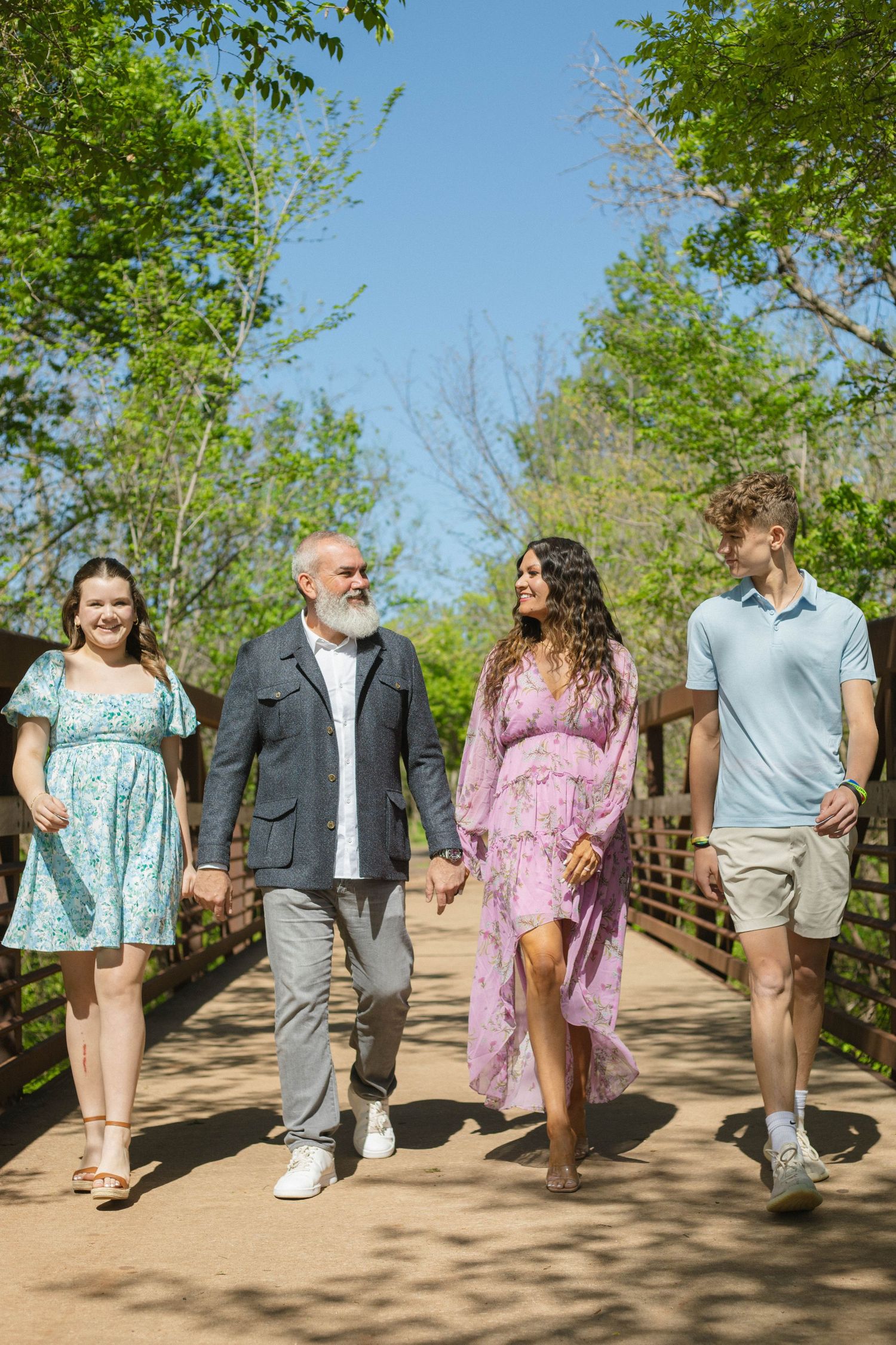 A sequence of candid walking shots showing people strolling together along a dirt path surrounded by green trees.