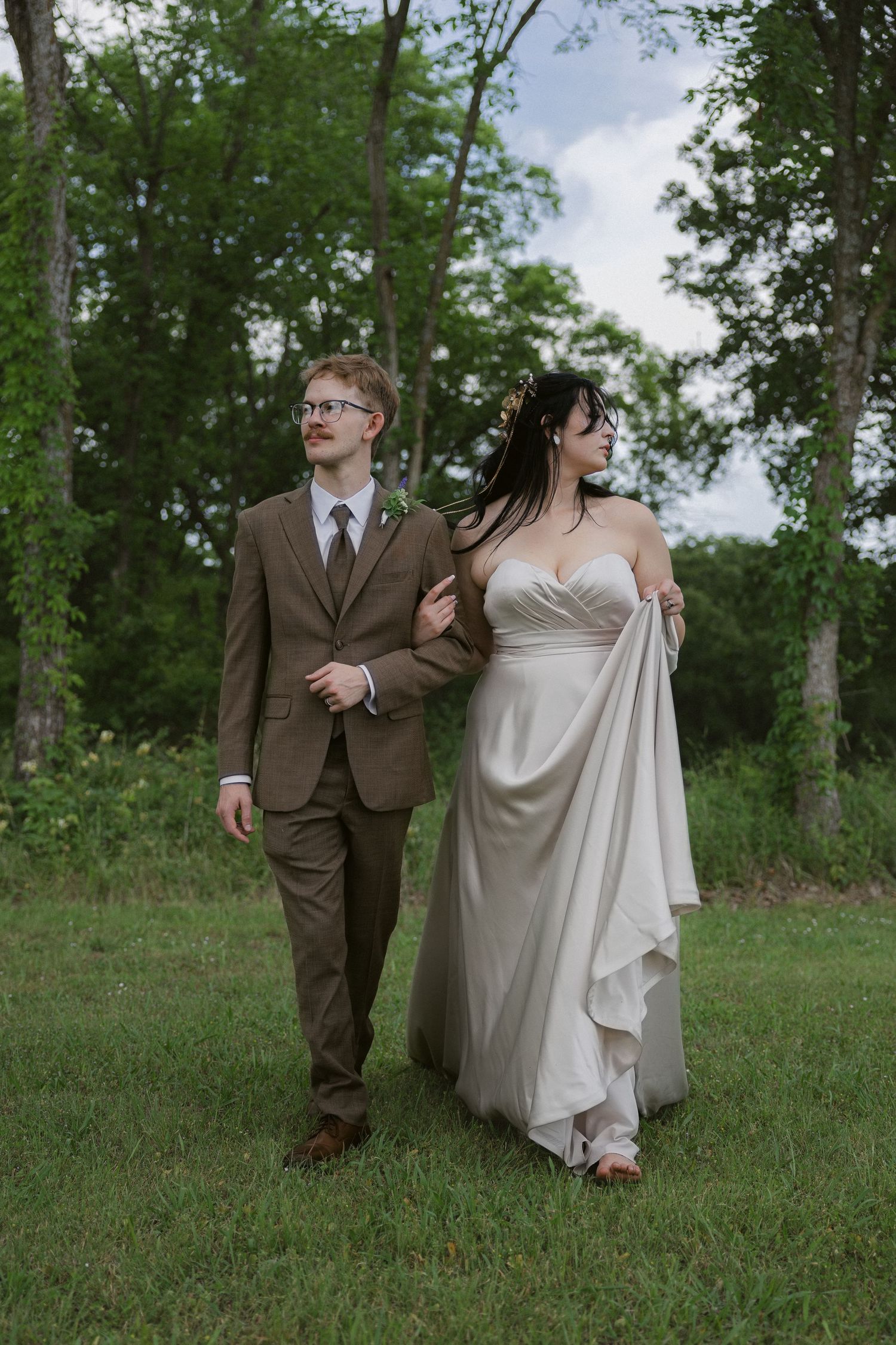 Couple walking and laughing together across a grassy hillside in formal attire.